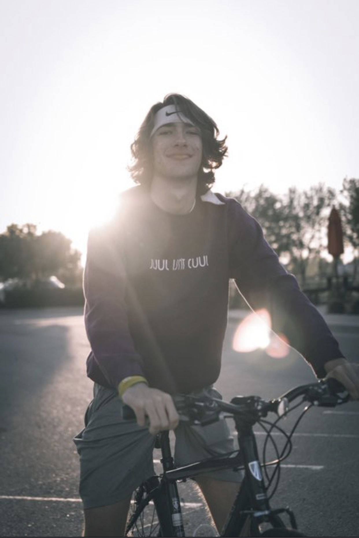 美國YouTuber Baylen Levine 騎行攝影 壁紙 — 一位戴著頭帶的年輕男子在陽光明媚的停車場中微笑著拿著一輛自行車，正值黃金時刻。