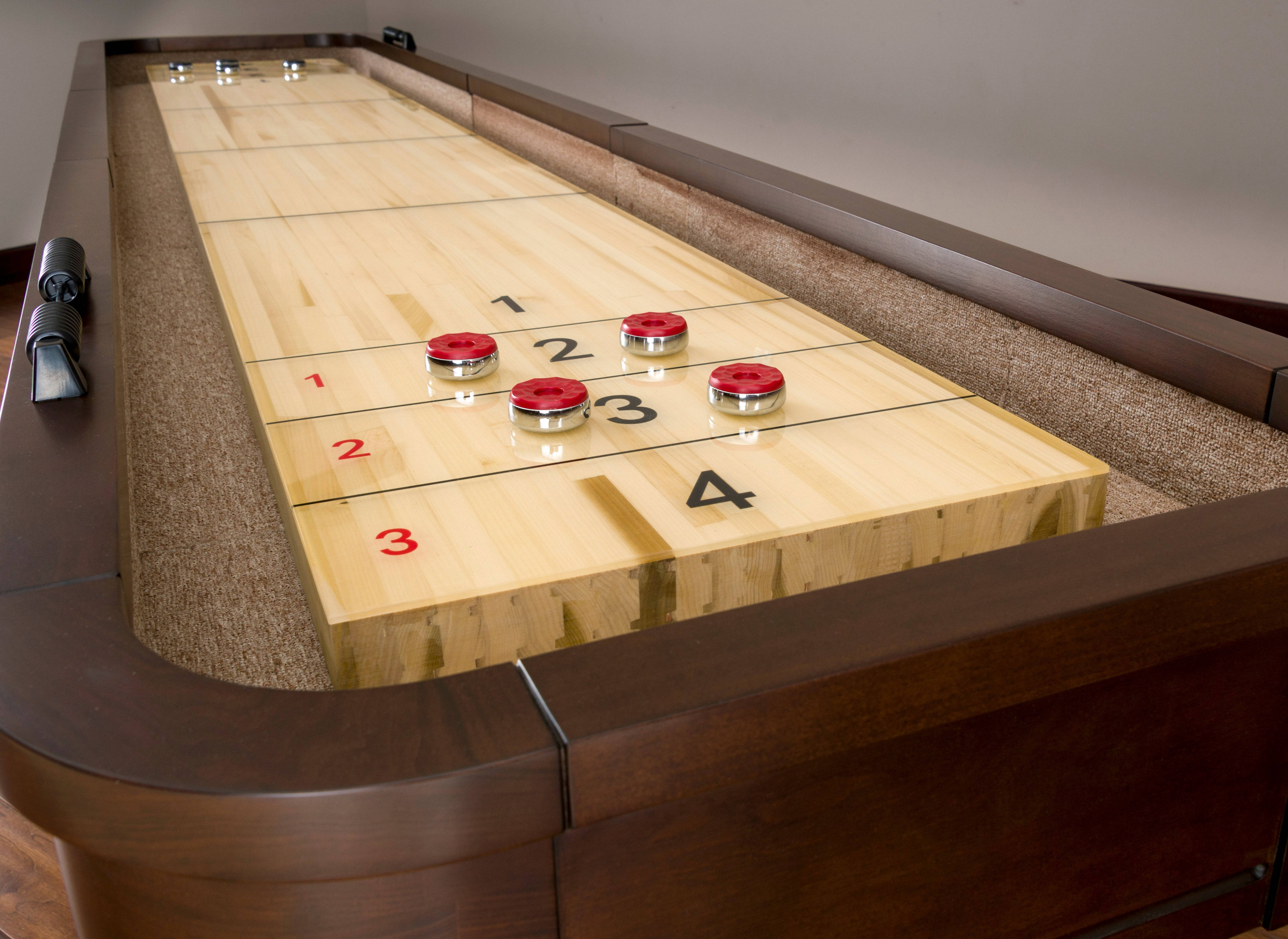 美國傳承米蘭 Shuffleboard 遊戲進行中 壁紙 — 一張拋光木製沙狐球桌，紅色冰球放在編號的球道上，以深色木材和米色地毯框住。