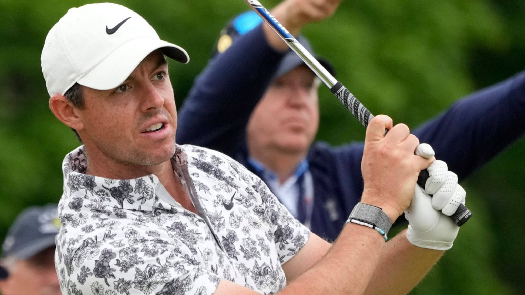 美國公開賽傳奇推桿手布拉德·法克森 壁紙 — 高爾夫球手 Rory McIlroy 揮桿中，身穿花卉圖案襯衫和白色帽子，背景為模糊的綠色。
