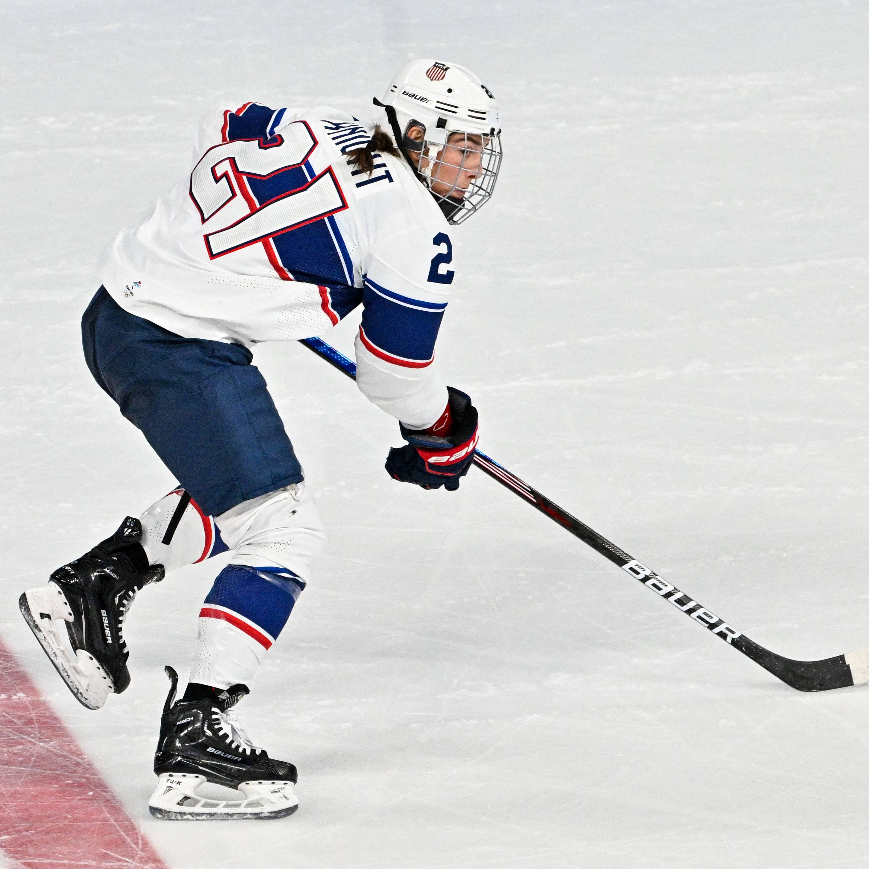 美國冰球隊 #21 Hilary Knight 壁紙 — 一位專注的冰球運動員身穿白色、藍色和紅色的裝備，在明亮的冰場上手持 Bauer 球桿激烈滑行。