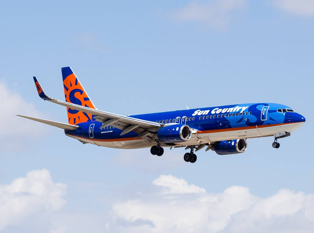 Sun Country Airlines 噴射機放下起落架，在部分多雲的天空中低飛。