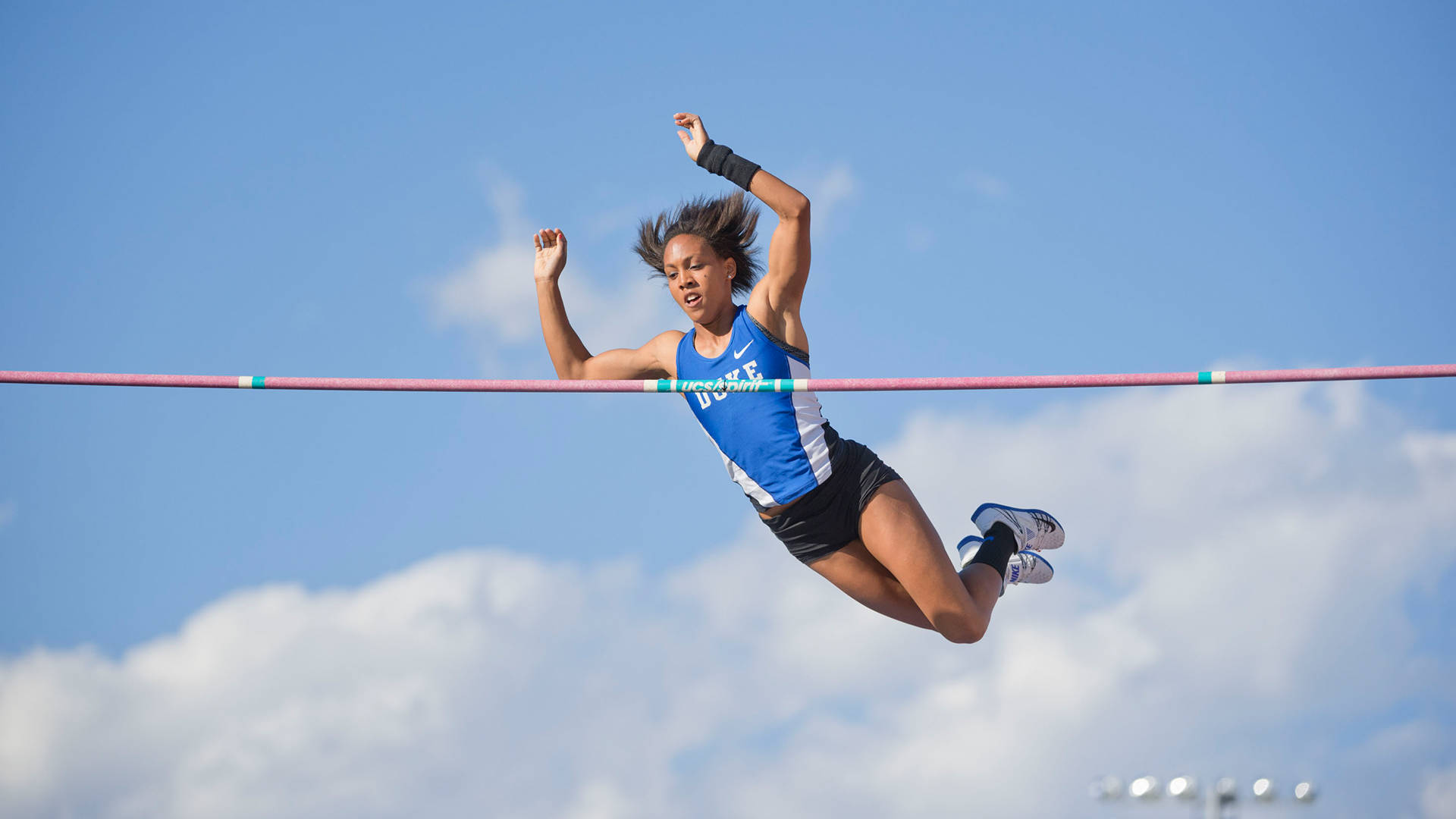 女運動員在半空中越過跳高橫桿，陽光明媚