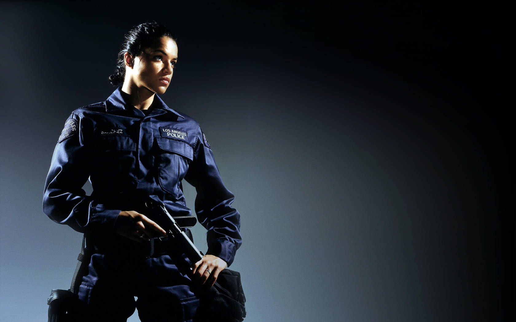 美國女演員米歇爾·羅德里格斯在《S.W.A.T.》 壁紙 — 一名身穿深色制服的警察在戲劇性的工作室燈光下，對著灰色漸變背景持槍擺出姿勢。