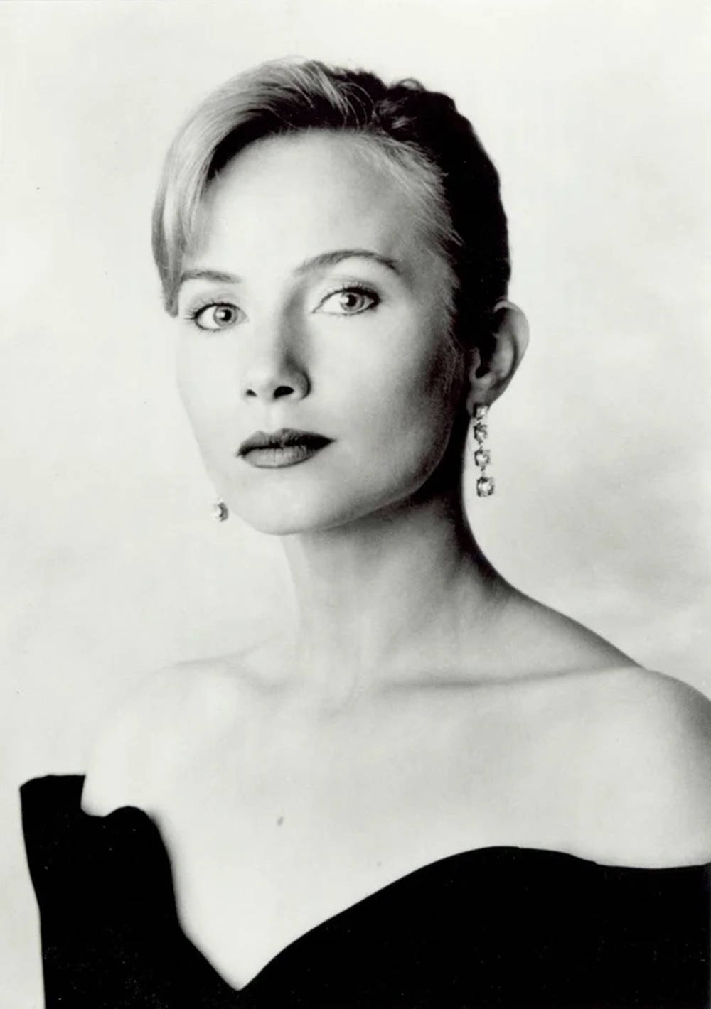 一位短髮女性戴著垂墜耳環和黑色露肩上衣的攝影棚肖像。