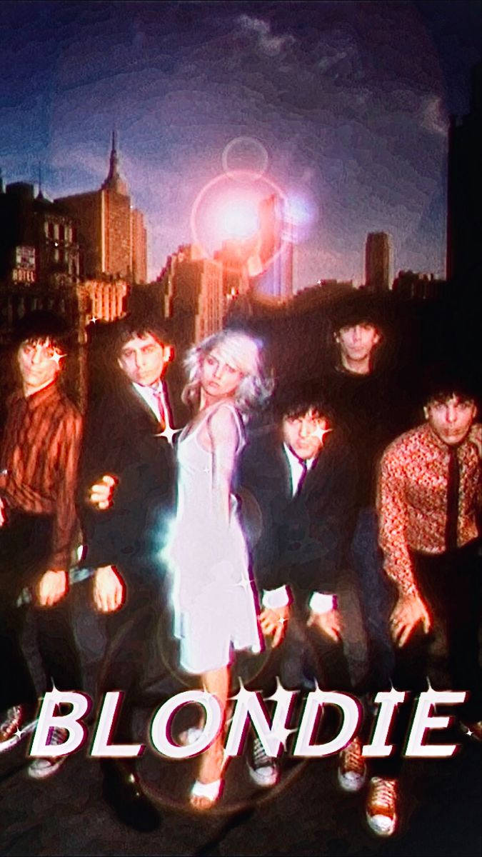 Blondie 樂隊成員在夜間霓虹燈照亮城市景觀前擺姿勢。