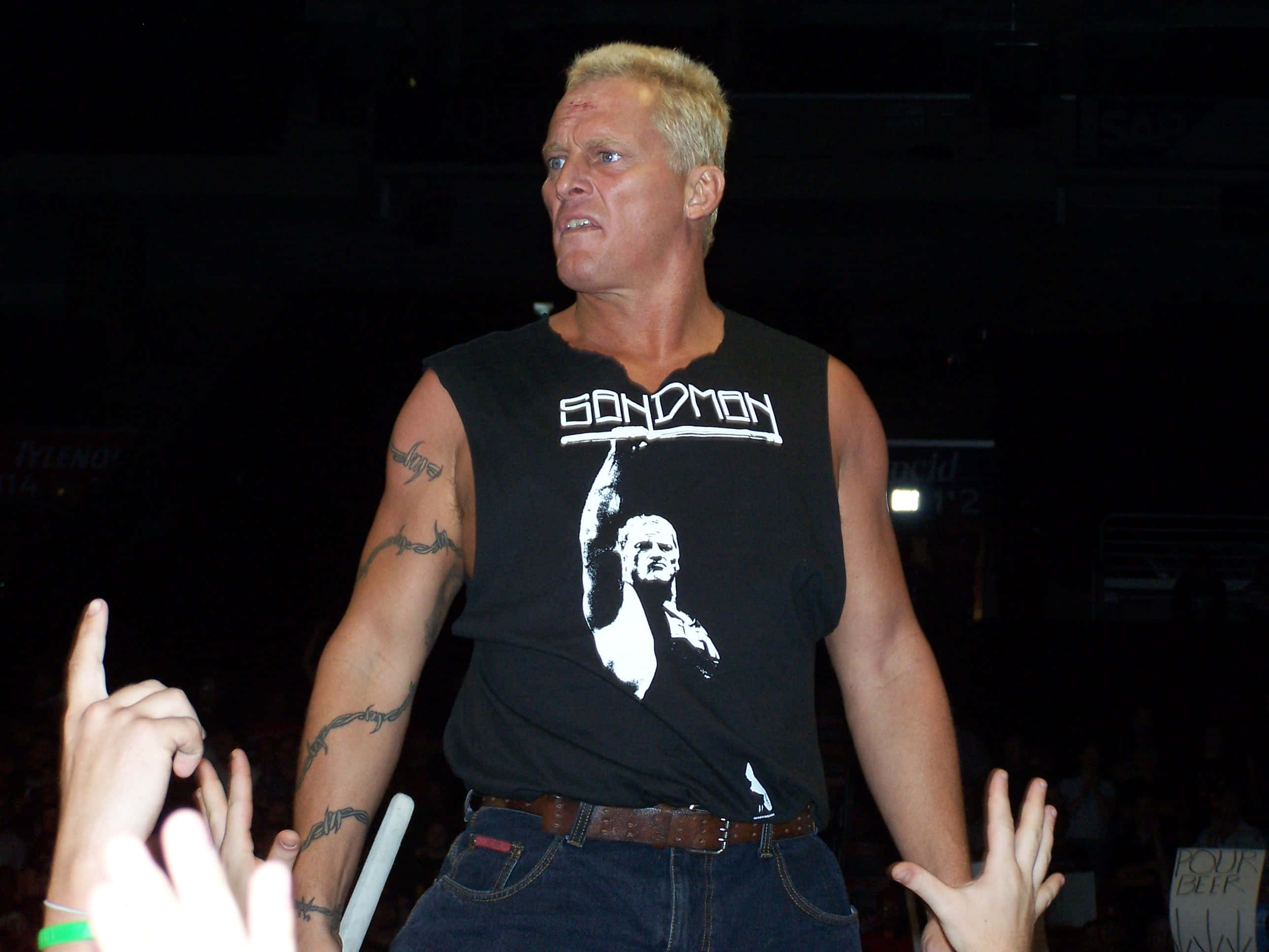 美國摔角手 The Sandman James Fullington ECW 2006 活動 壁紙 — 一個肌肉發達、金髮、有紋身的男人穿著黑色 'BOND MAN' 背心，在燈光昏暗的場館與粉絲互動。