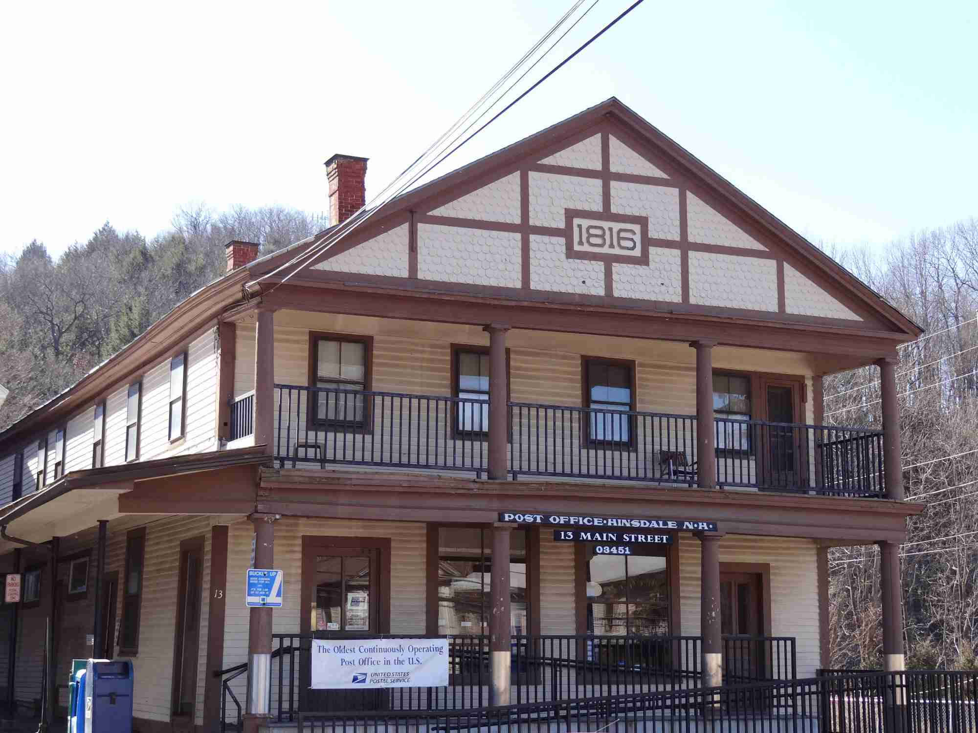 美國最古老郵政局 壁紙 — 一座建於1816年的歷史郵局建築，擁有木質牆板和陽台，矗立在晴朗的天空下，背景是光禿禿的樹木。