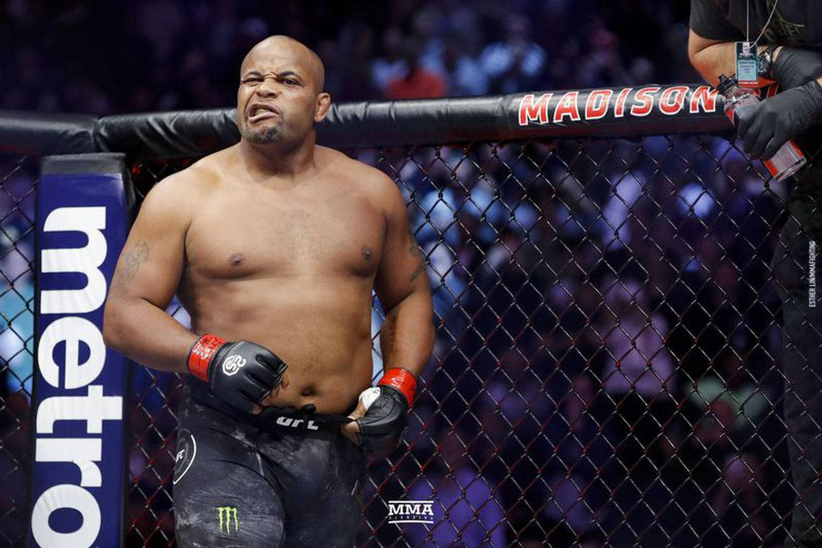 美國格鬥家丹尼爾·科爾米爾 UFC 210 壁紙 — 一位肌肉發達的MMA拳手在明亮的場館燈光下，於籠中比賽時面露苦相。