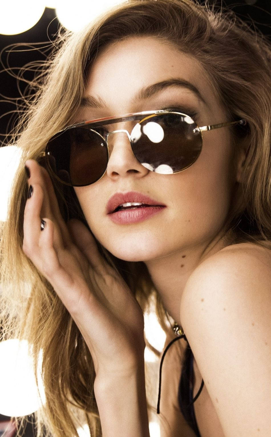 美國模特 Gigi Hadid 穿 Tommy Hilfiger 壁紙 — 一位金髮魅力女性戴著時尚太陽眼鏡，在明亮的攝影棚燈光背景下擺姿勢。