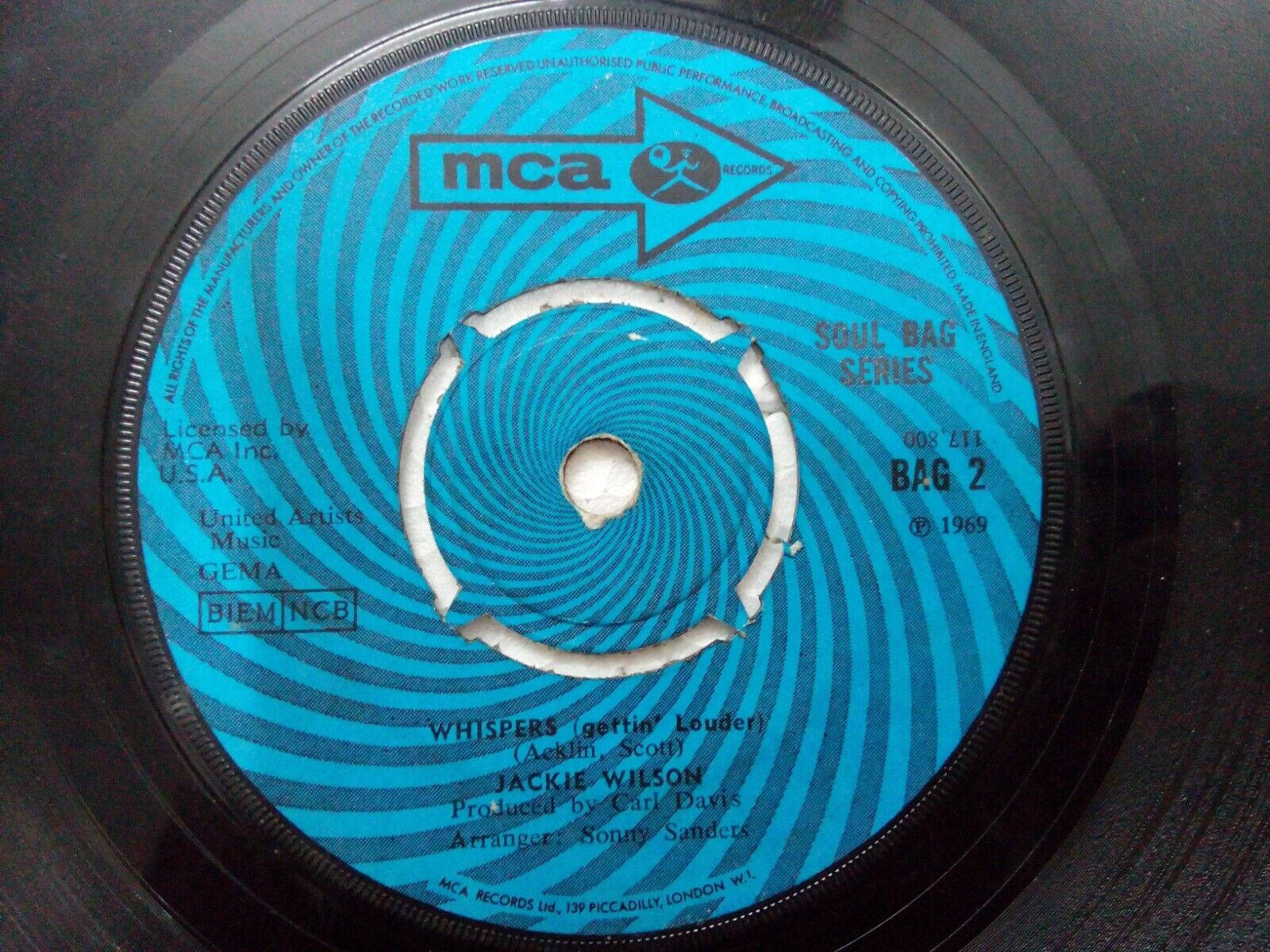 美國歌手Jackie Wilson的黑膠唱片 壁紙 — 一張1969年MCA復古唱片標籤，帶有催眠般的藍色螺旋設計和白色中心孔。