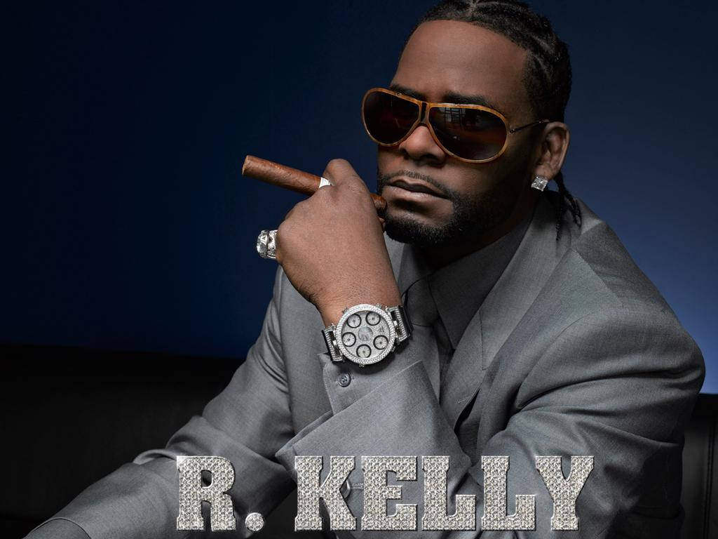 R Kelly身穿灰色西裝，手持雪茄，佩戴鑲鑽手錶和太陽眼鏡。