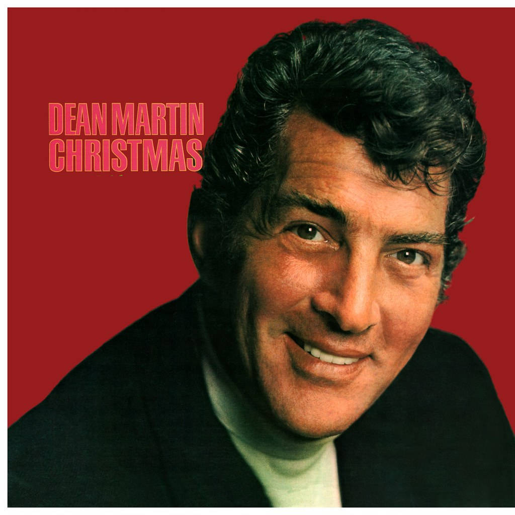 甸·馬田穿著黑色西裝微笑，紅色背景上粉紅色文字寫著 Dean Martin Christmas。