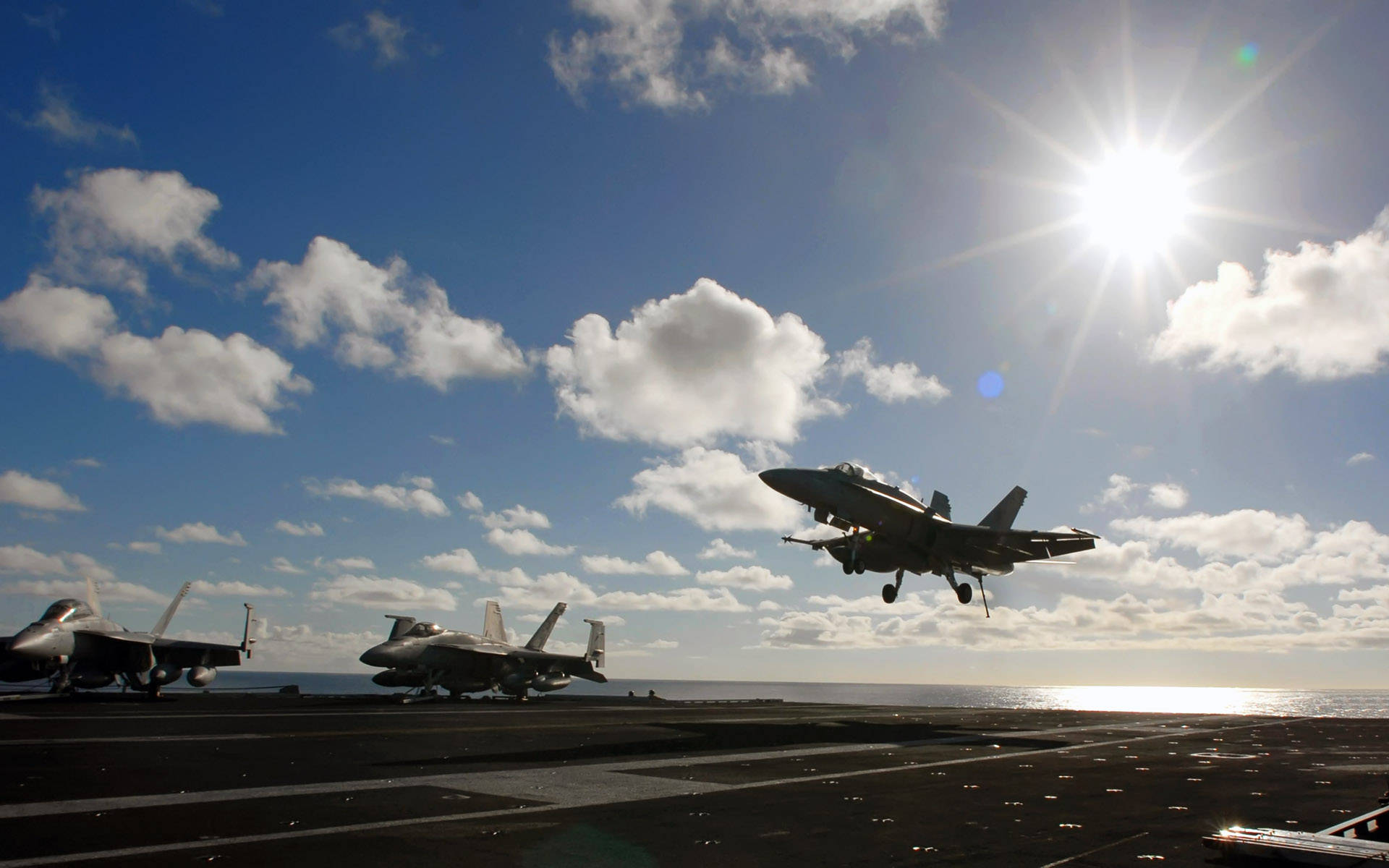 美國海軍空軍 壁紙 — 一架戰鬥機從航空母艦甲板起飛，陽光燦爛，雲朵散落，海平線清晰可見。