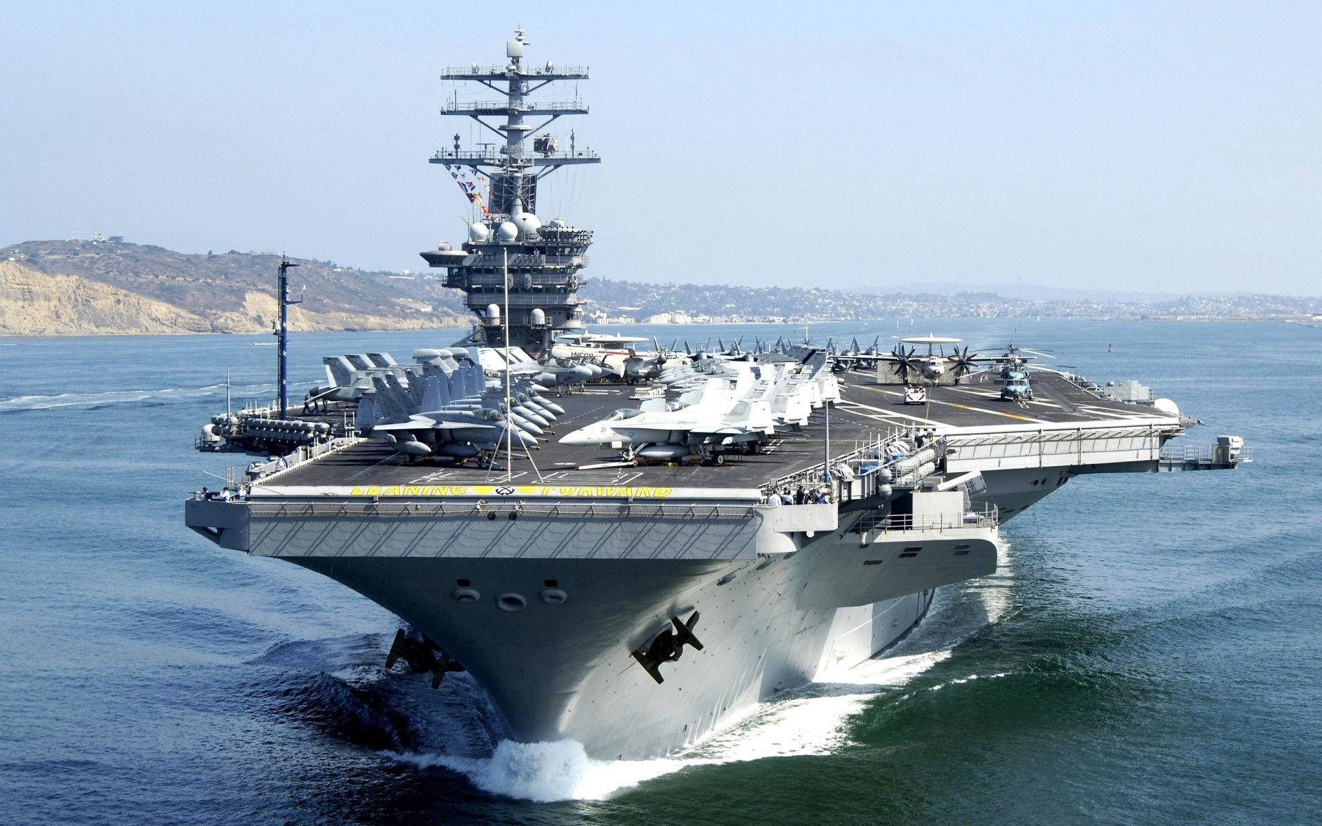 美國海軍航空母艦滿載飛機 壁紙 — 一艘巨大的灰色航空母艦在藍色海洋中航行，戰鬥機整齊排列在甲板上，天空晴朗。