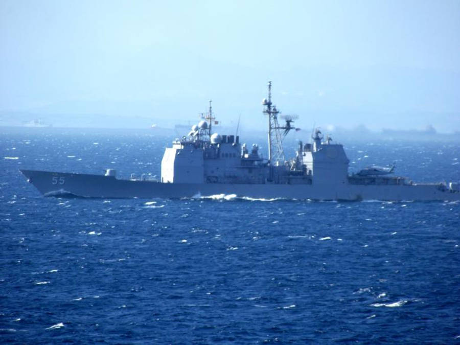 美國海軍艦艇航行於地中海 壁紙 — 一艘灰色海軍驅逐艦在朦朧的天空下劃過深藍色的海洋波浪，遠處可見陸地。