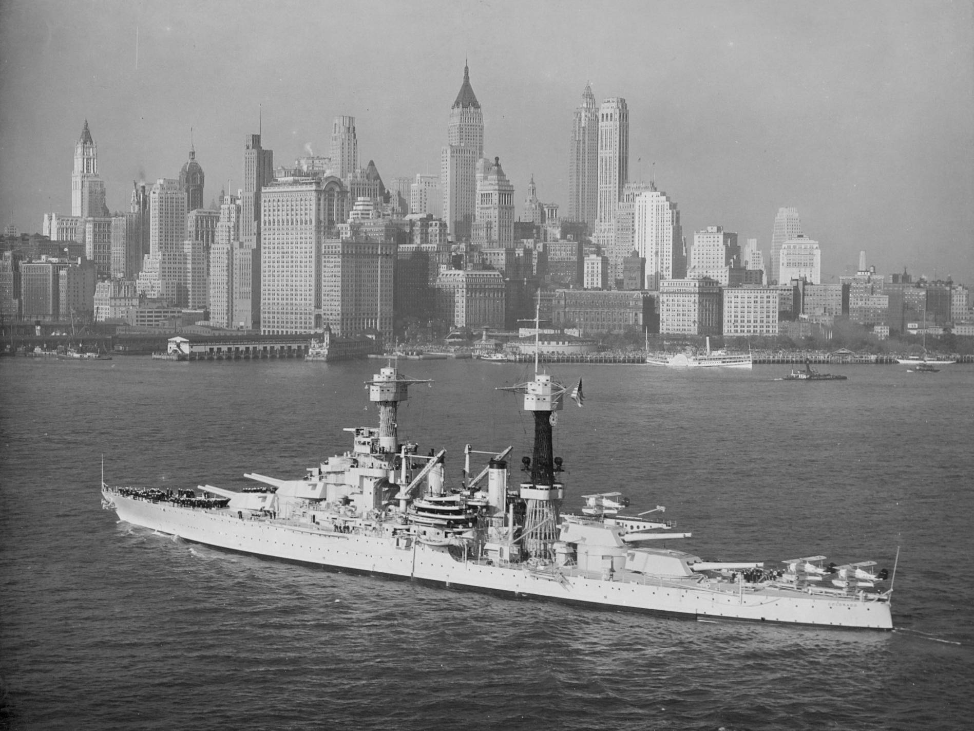 美國海軍艦艇航行於紐約 壁紙 — 一艘歷史戰艦駛過港口水域，背景是早期摩天大樓密集的城市天際線。