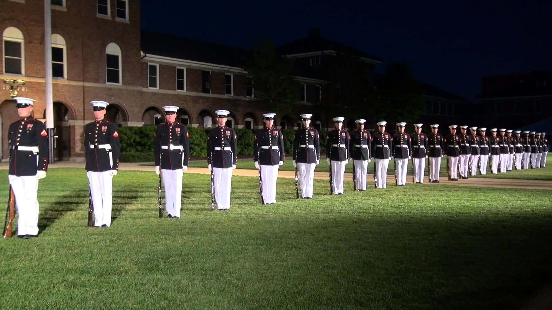 身穿禮服的海軍陸戰隊員在夜間的草地上以直線立正。
