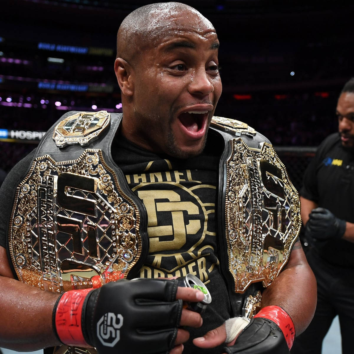 美國混合格鬥家丹尼爾·科爾米爾 壁紙 — 一位勝利的MMA拳手在燈光明亮的競技場中，肩上披著閃閃發光的冠軍腰帶慶祝勝利。