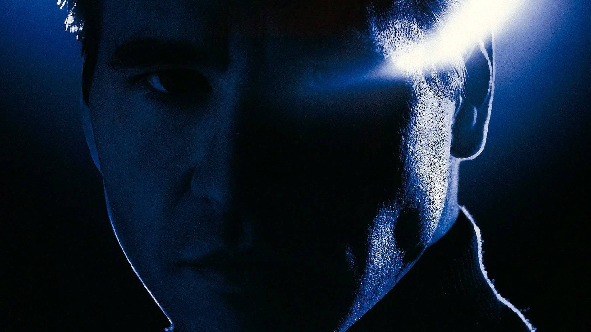 美國演員 Val Kilmer 創意海報 壁紙 — 一個男人的臉被側面明亮的藍色光戲劇性地照亮，背景是黑暗的。