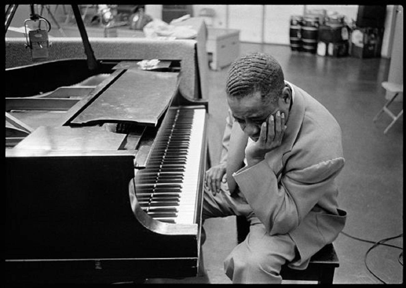 美國爵士鋼琴家 Art Tatum 單色肖像 壁紙 — 一張黑白照片，一名身穿西裝的男子坐在三角鋼琴前，在攝影棚內將頭靠在手上。