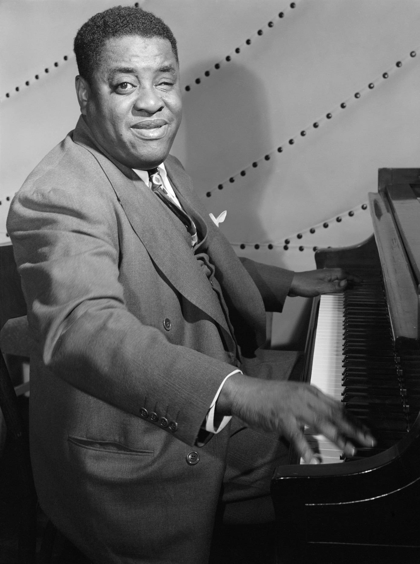 美國爵士鋼琴家 Art Tatum 古董照片 壁紙 — 一位身穿西裝、微笑的爵士鋼琴家，在圓點背景前彈奏三角鋼琴，經典黑白工作室肖像。