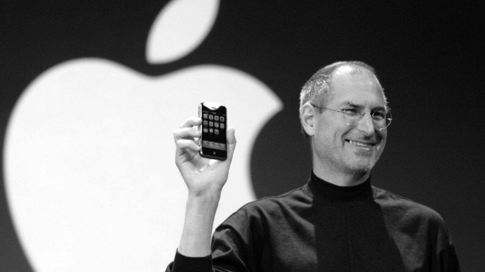 史提夫·喬布斯在舞台上展示第一部iPhone，身後有Apple標誌。