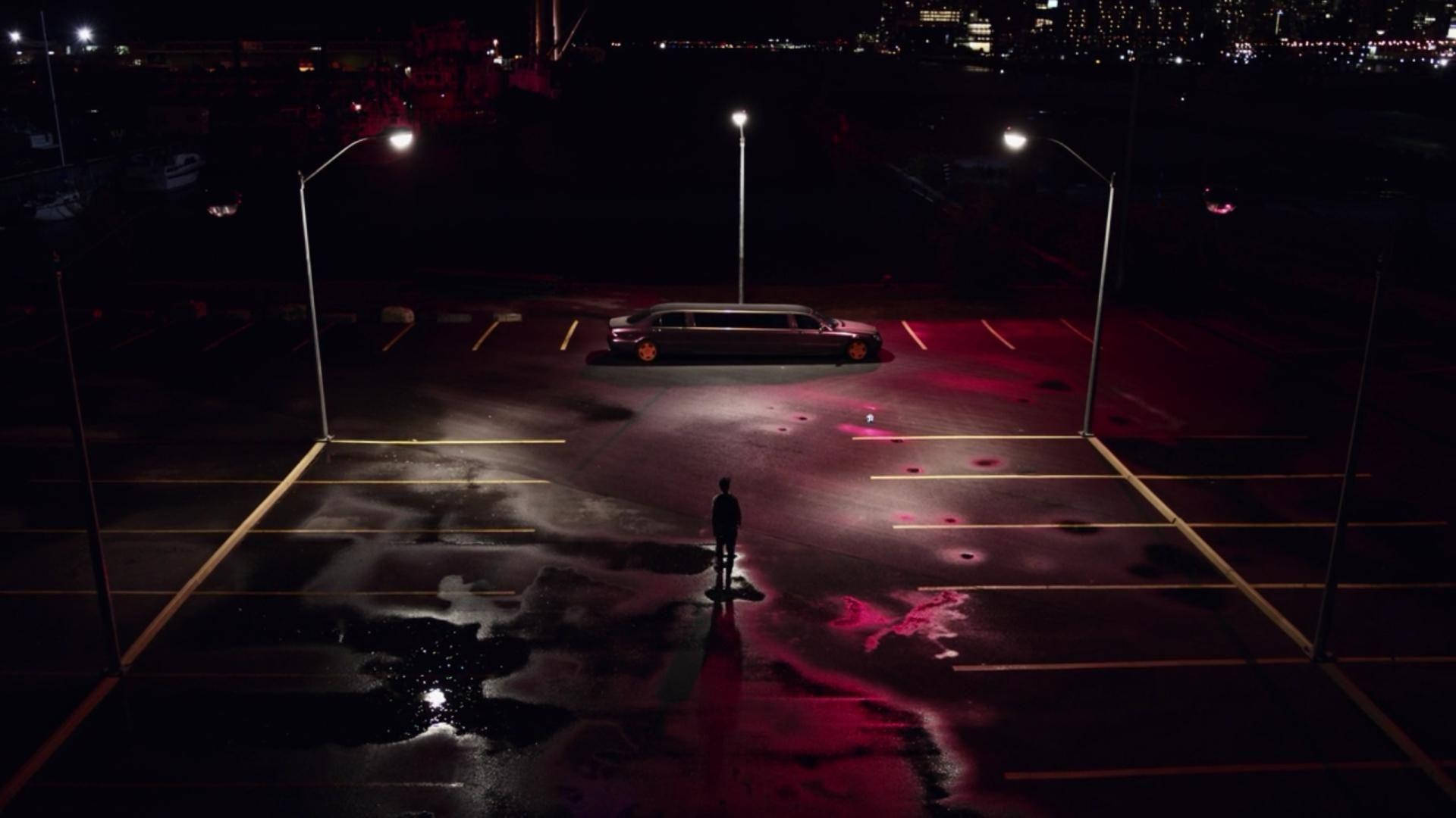 一個人在夜晚潮濕的停車場靠近豪華轎車站立的剪影。
