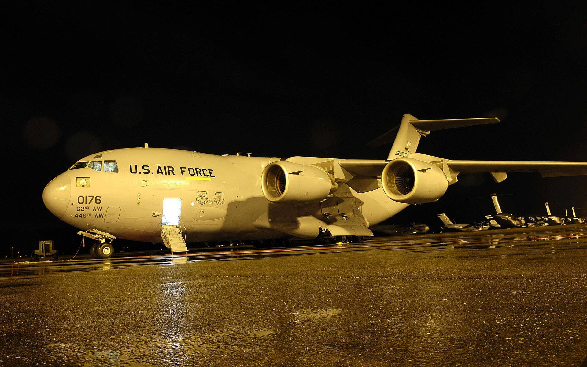 美國空軍 Globemaster 夜間 壁紙 — 一架美國空軍貨機在漆黑的夜空下，被溫暖的燈光照亮在潮濕的停機坪上。