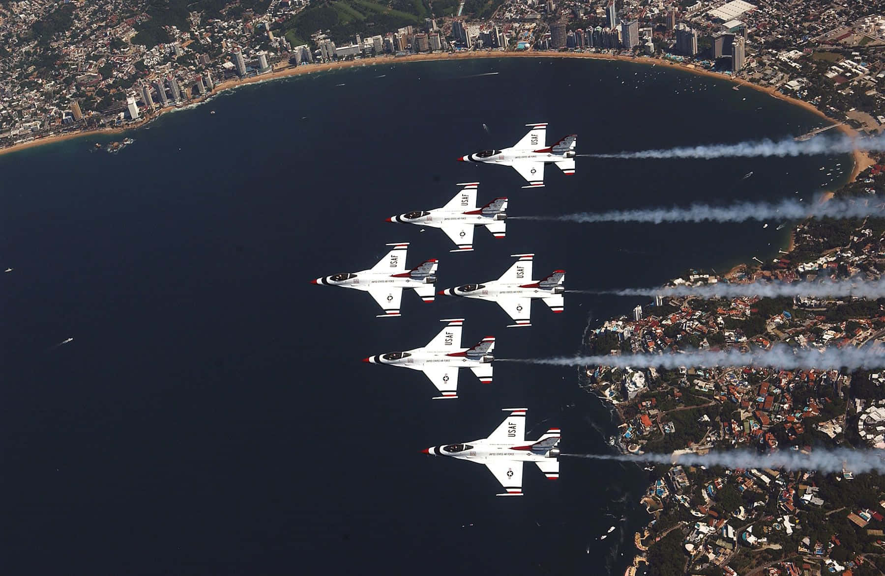 五架戰鬥機以編隊飛越沿海城市，帶有煙跡。