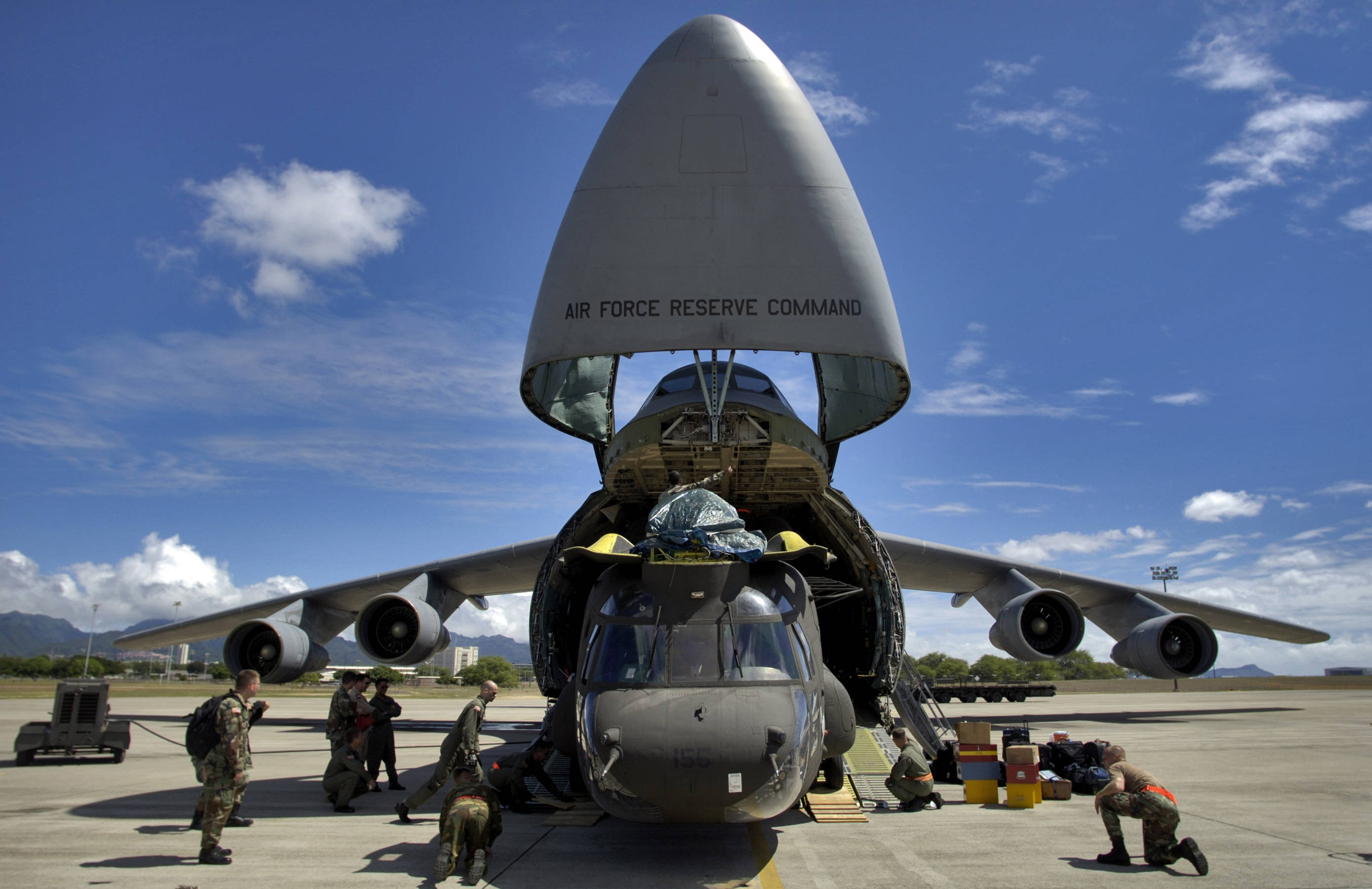 美國空軍銀河號 壁紙 — 軍方人員在明亮的藍天下，將一架直升機裝載到一架巨大的空軍預備役司令部運輸機的開放貨艙中。