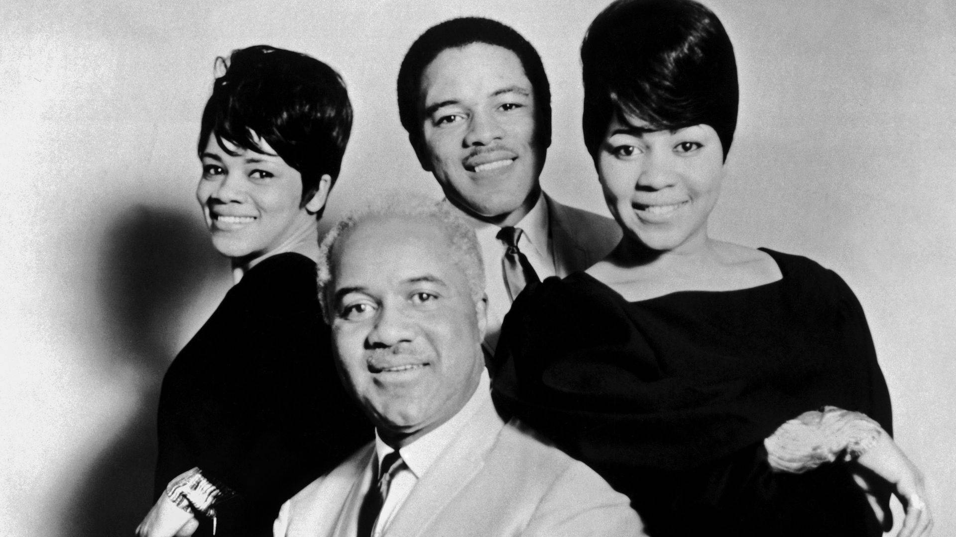 美國組合Staple Singers 1965年肖像照 壁紙 — 四位微笑的音樂家緊密地擺姿勢，拍攝經典黑白工作室肖像，光線柔和，陰影戲劇化。