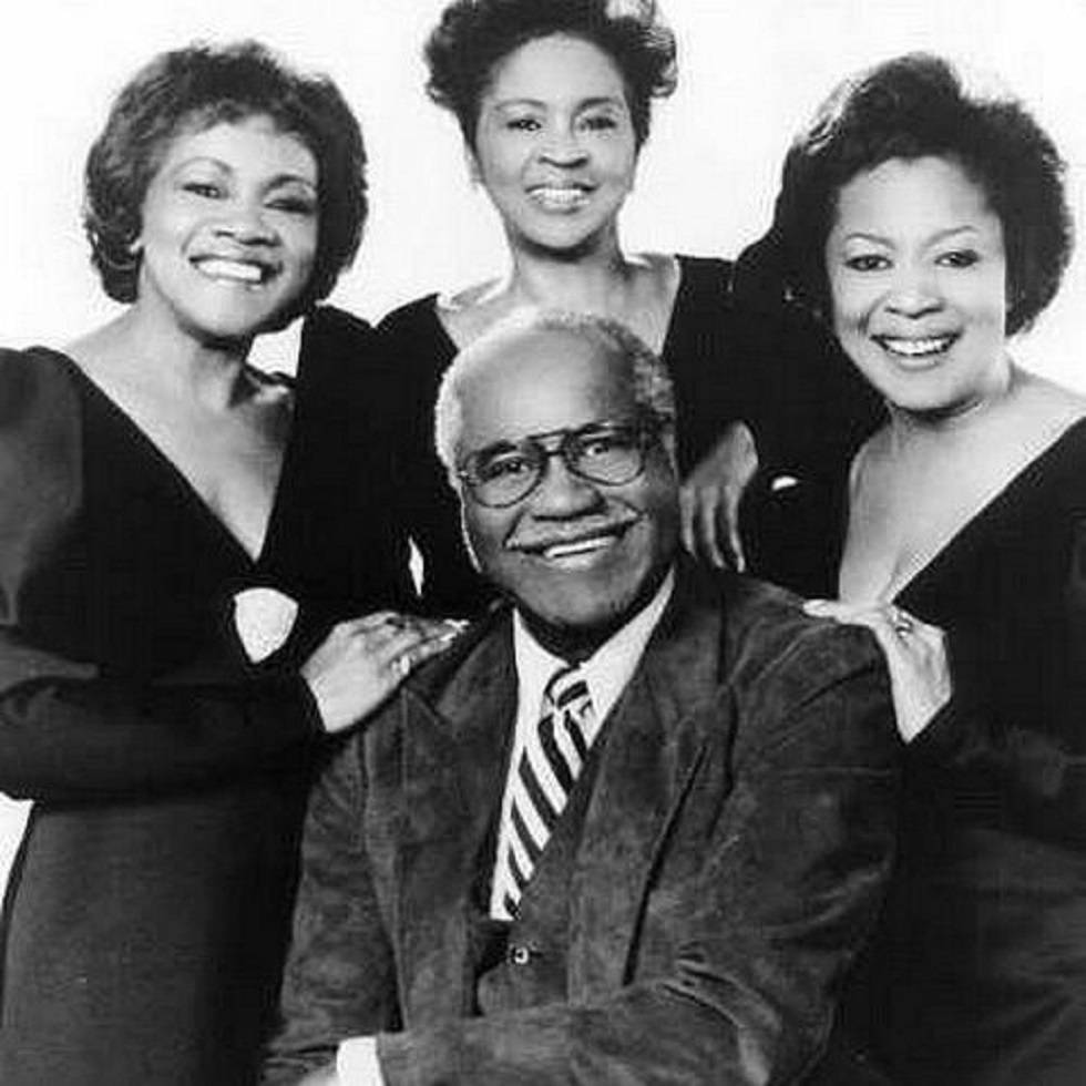 美國組合Staple Singers 1985年肖像照 壁紙 — 一張快樂的黑白肖像照，四個微笑的人緊密地靠在一起，手臂互相環繞。