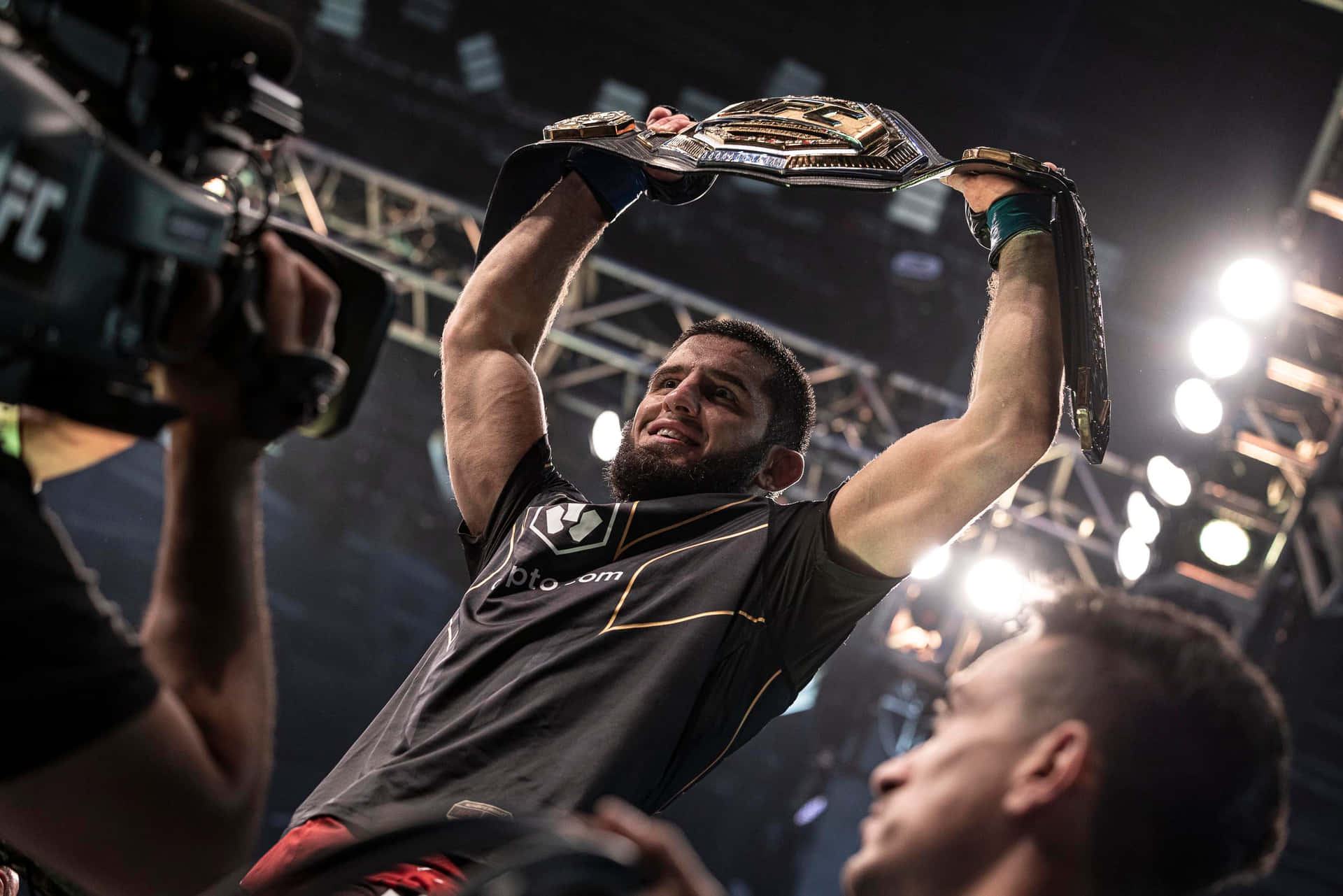美國綜合格鬥選手 Evan Tanner — 前中量級冠軍 壁紙 — 一位勝利的UFC拳手在明亮的場館燈光下高舉冠軍腰帶，相機捕捉了這一刻。
