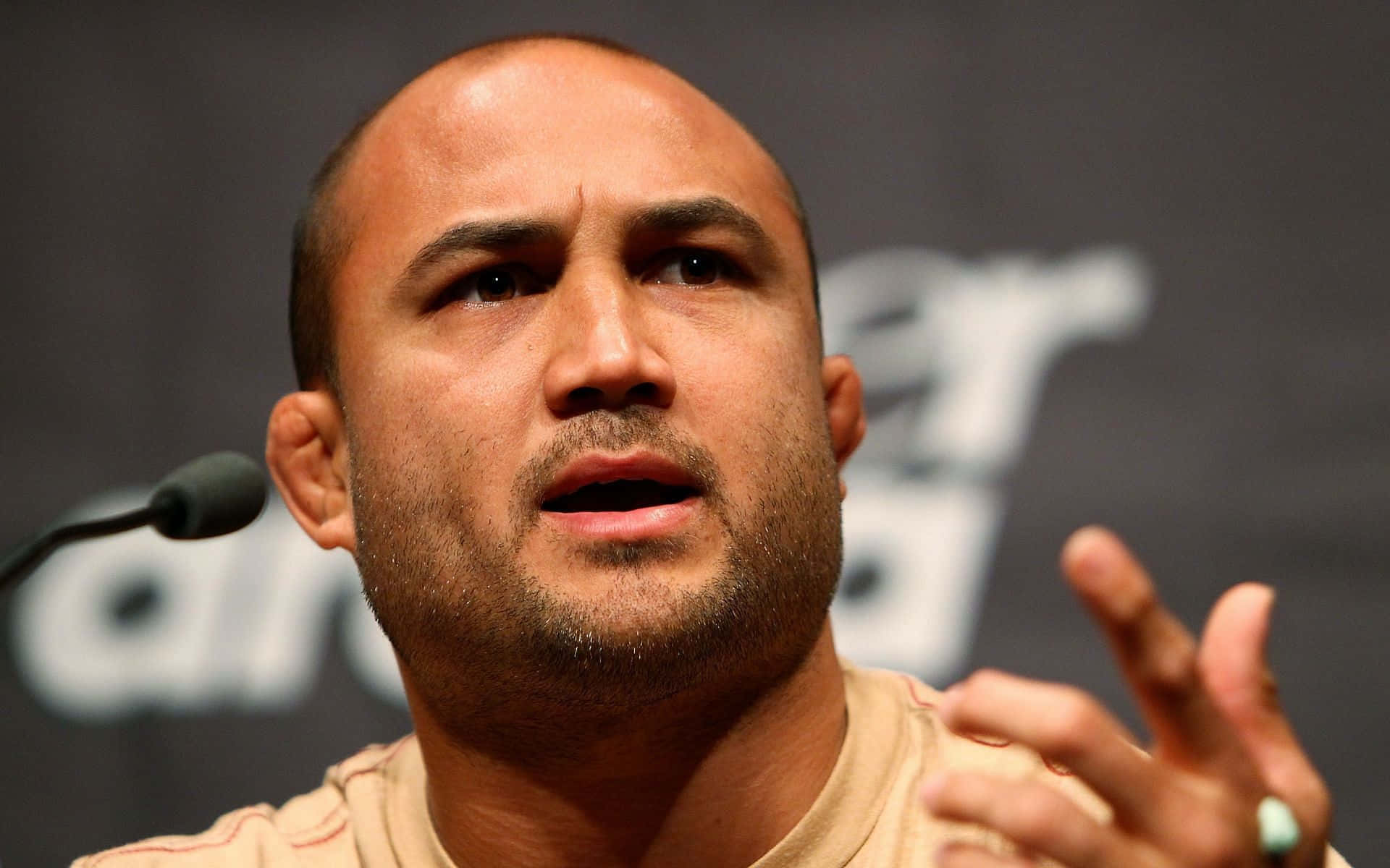 美國綜合格鬥選手BJ Penn 壁紙 — 禿頭鬍鬚男在記者會上拿著咪高峰熱情演講的特寫。