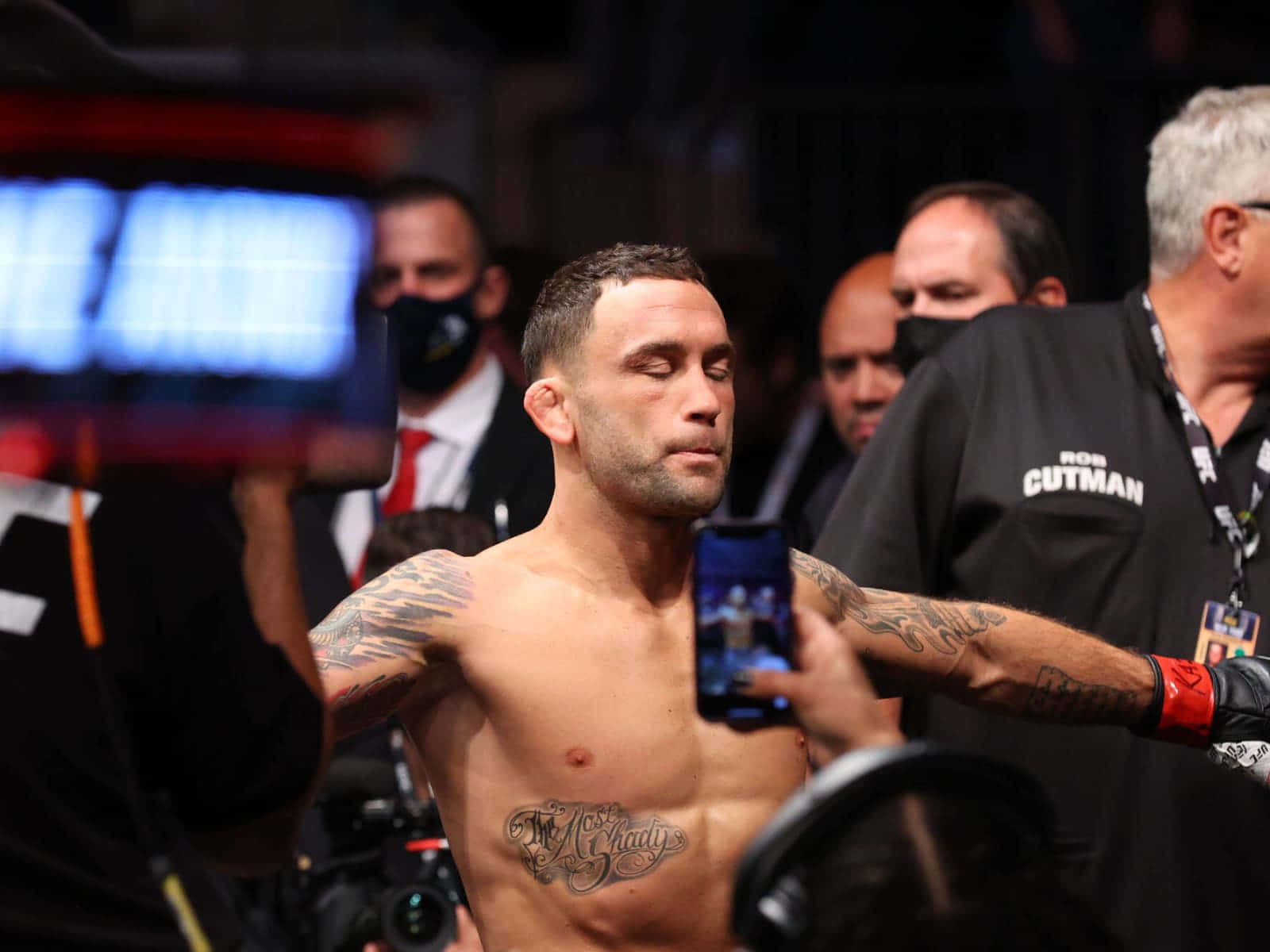 美國綜合格鬥選手弗蘭基·愛德加於UFC 268賽事亮相 壁紙 — 一位紋身嘅戰士喺昏暗嘅競技場赤裸上身企喺度，粉絲同工作人員用手機同相機包圍佢。