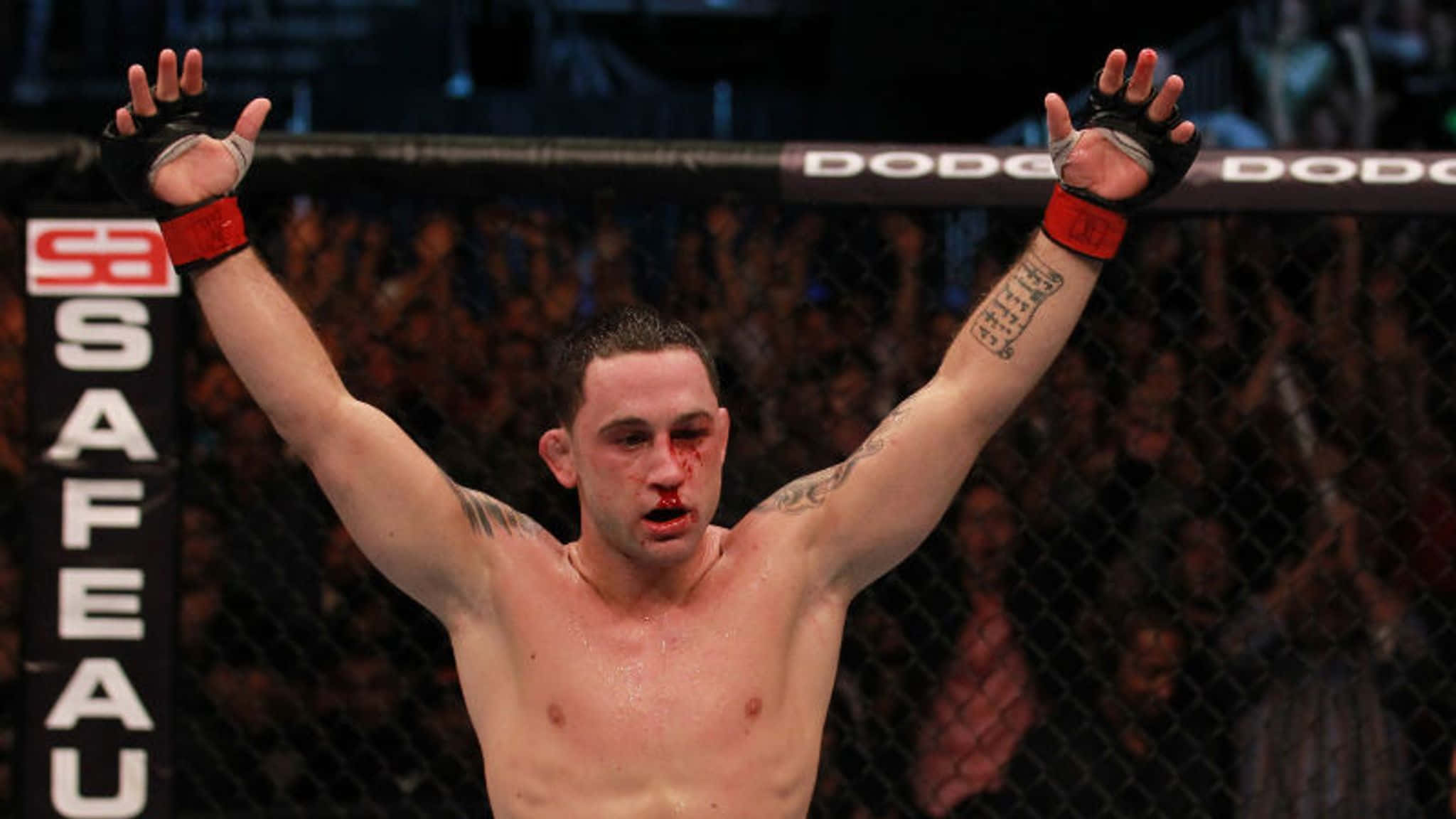 美國綜合格鬥選手弗蘭基·愛德華於 UFC 136 壁紙 — 一名血跡斑斑的MMA拳手在籠內高舉雙臂慶祝勝利，身後是歡呼的人群。