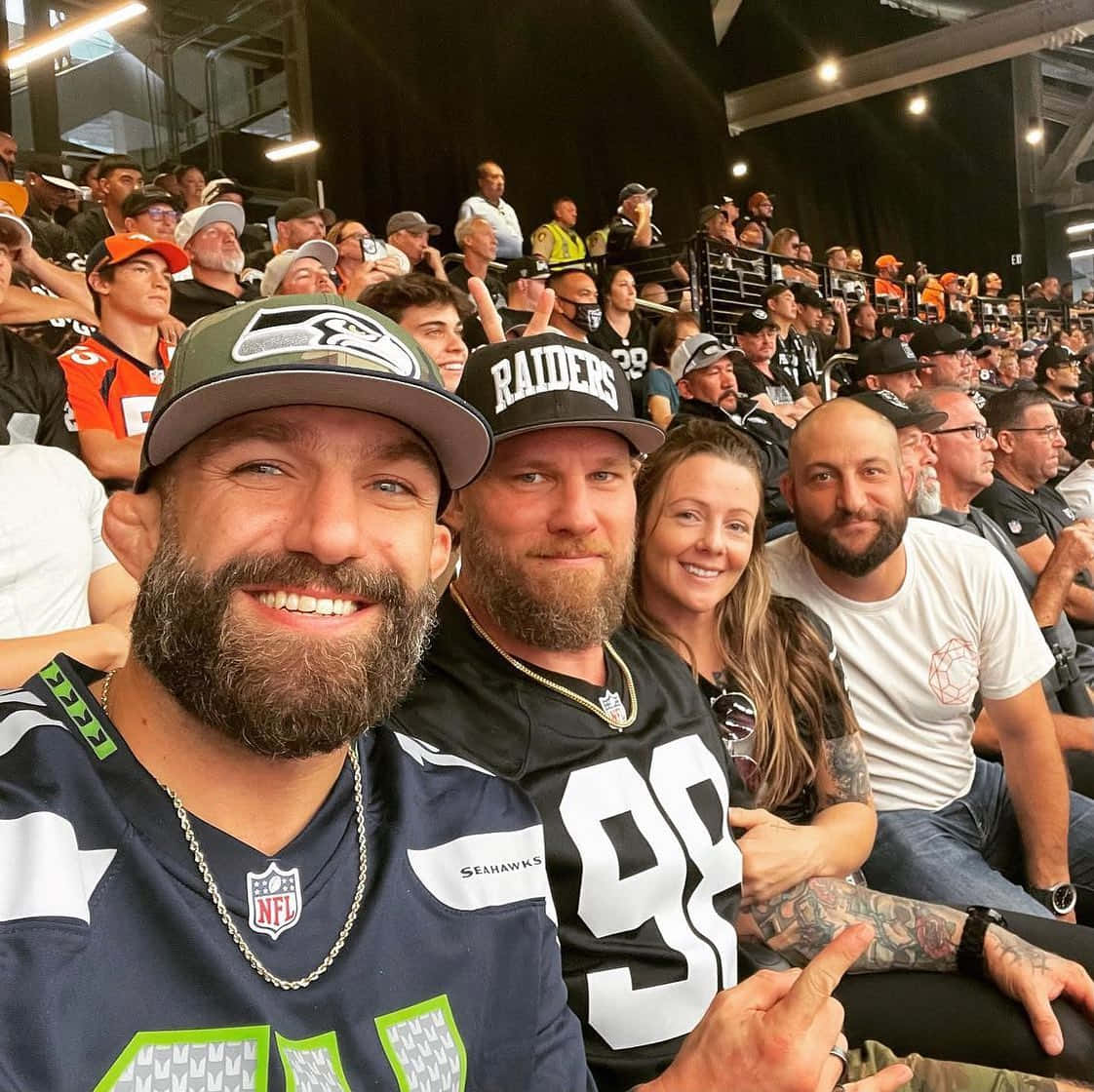 四名留鬍鬚的球迷身穿NFL球衣在體育館內微笑。