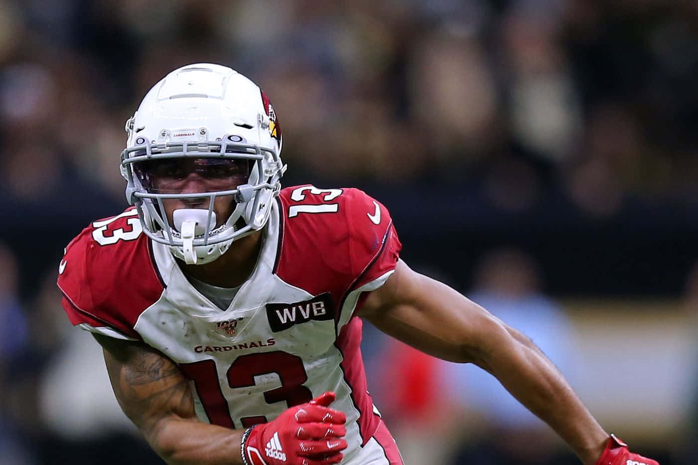 美國美式足球員克里斯蒂安·柯克比賽 壁紙 — 一名身穿紅白 Cardinals 裝備的美式足球員在球場燈光下比賽時，全神貫注地向前衝刺。