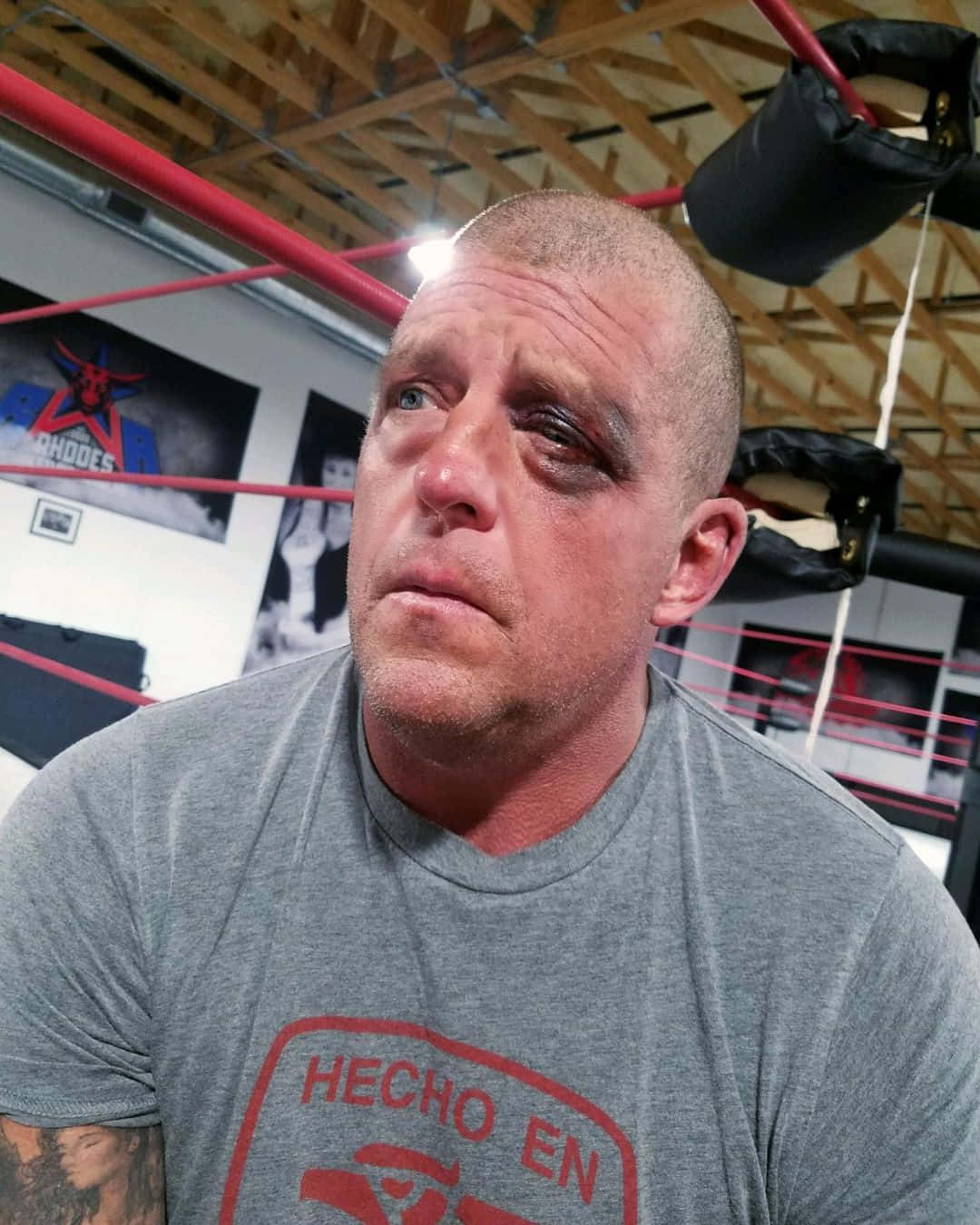 美國職業摔角手 Dustin Rhodes 近距離特寫 壁紙 — 一名瘀傷的摔角手，眼睛瘀黑，坐在擂台上，穿著灰色T恤，上面有紅色文字。