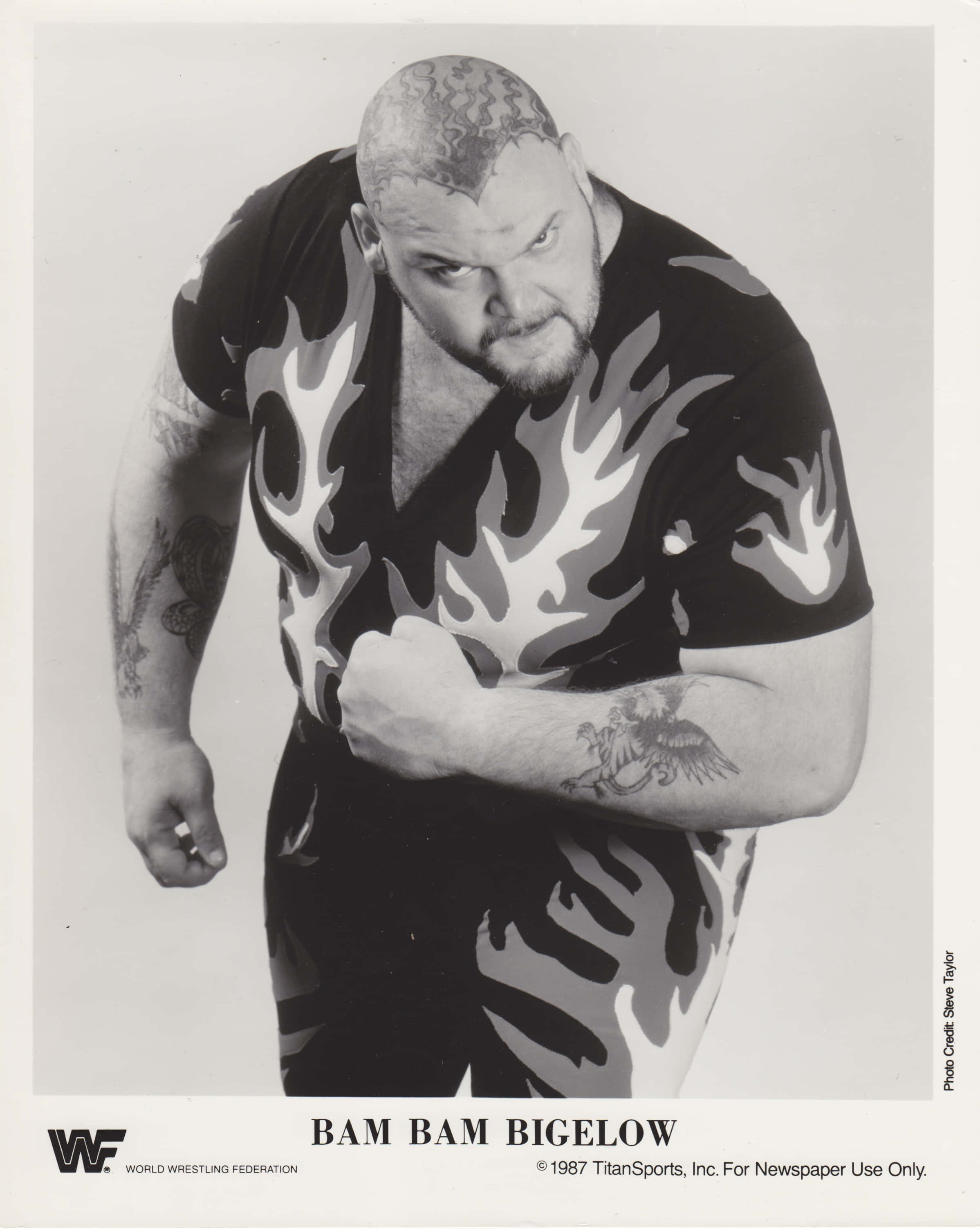 美國職業摔角手Bam Bam Bigelow復古WWE收藏卡 壁紙 — 一位肌肉發達的摔角手穿著火焰圖案襯衫和紋身，在黑白工作室肖像中凝視著鏡頭。