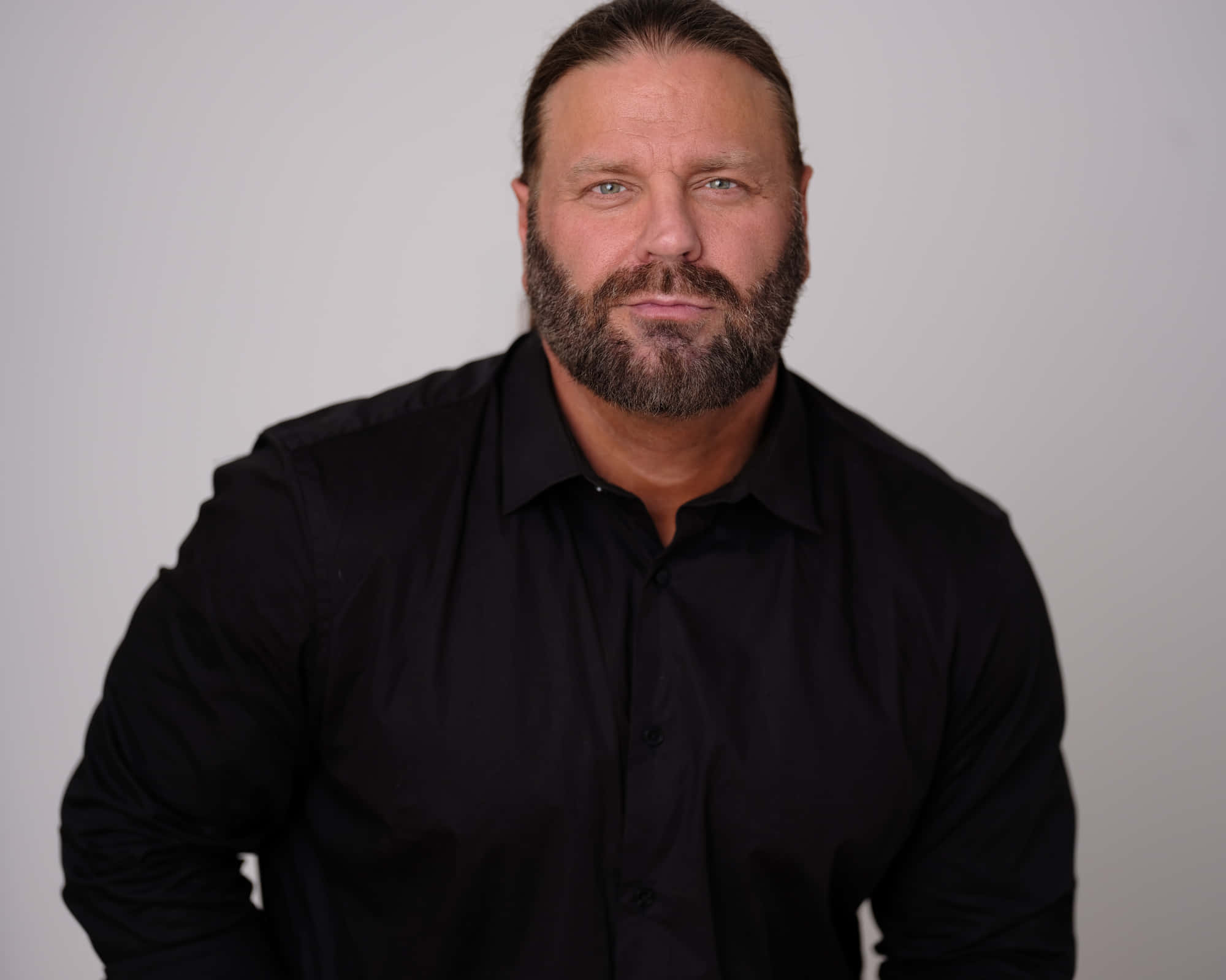 美國職業摔角手James Storm穿黑色扣釦襯衫 壁紙 — 一個肌肉發達、留著濃密鬍鬚的男人，穿著黑色鈕扣襯衫，背景是純白色。