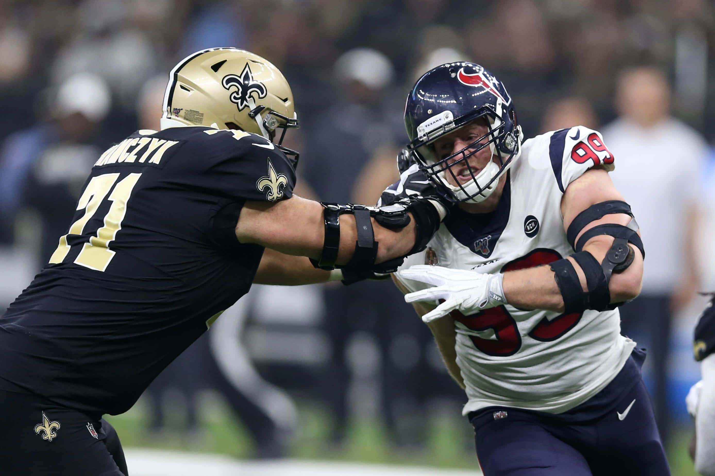 美國職業美式足球員Ryan Ramczyk擋下休士頓德州人隊J.J. Watt 壁紙 — 兩名NFL進攻鋒線球員在球場燈光下的一場比賽中激烈碰撞，進行激烈的身體對抗。