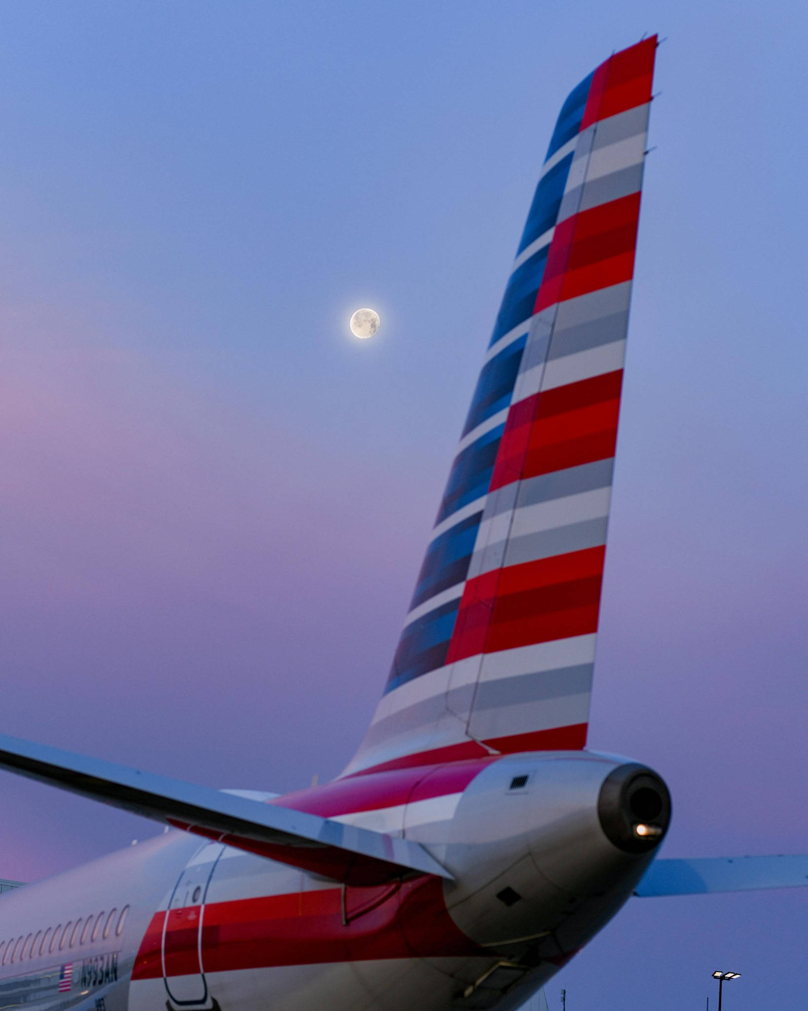 美國航空晨曦月影 壁紙 — 美國航空飛機尾部，帶有紅白藍條紋，背景為暮色天空和滿月。