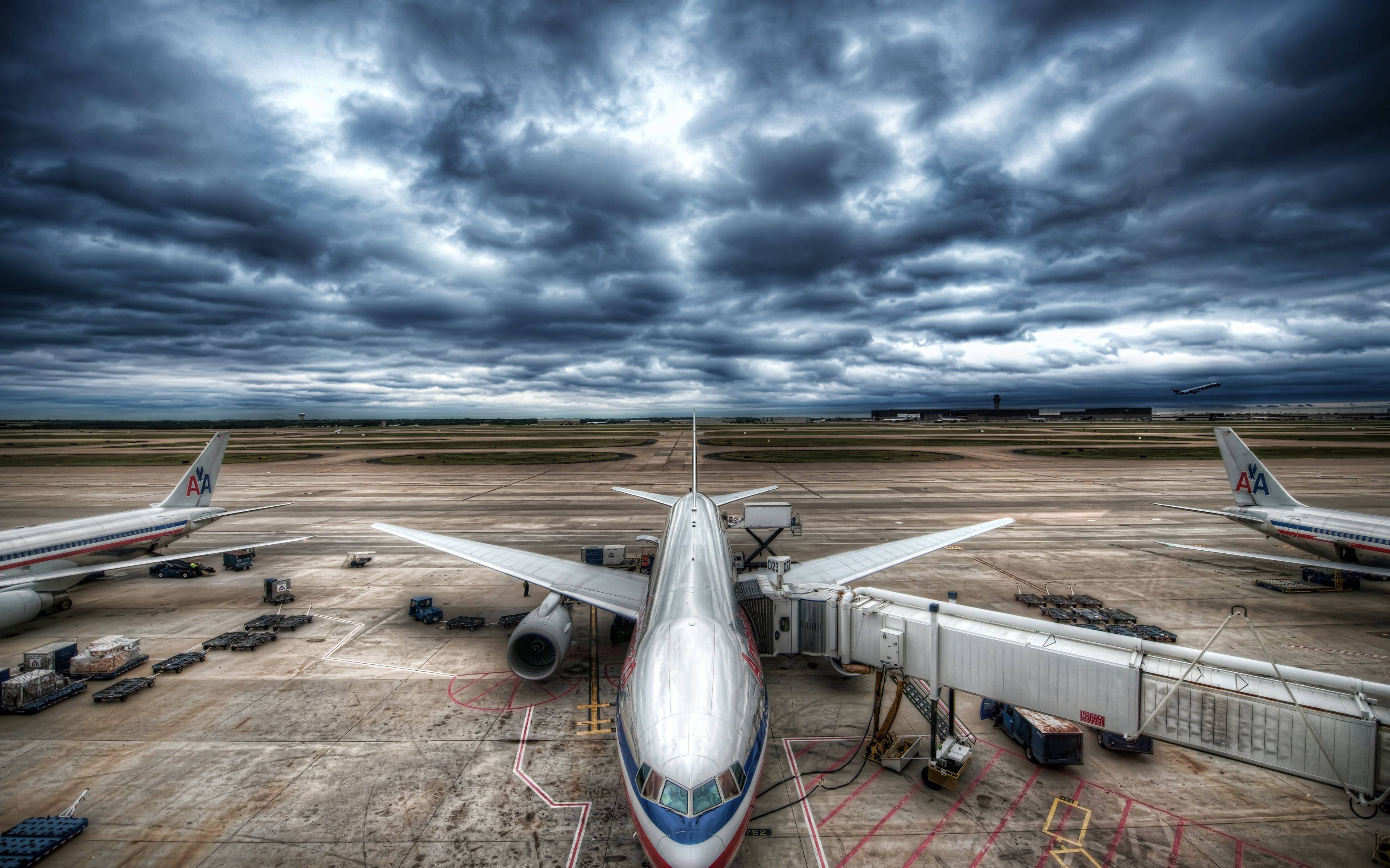 美國航空飛機在機場 壁紙 — 一架大型美國航空噴射機停在登機閘口，機場停機坪上空是戲劇性的暴風雨天氣。