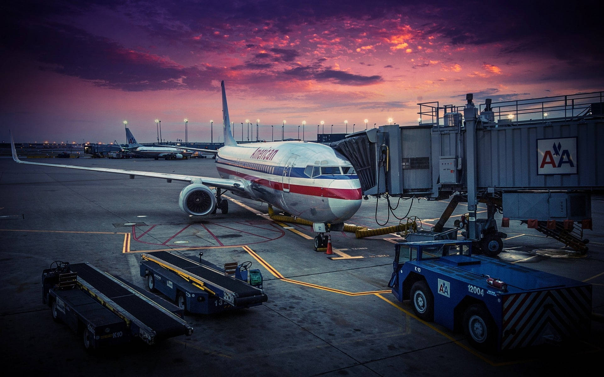 美國航空飛機在暮色中停在機場登機閘口，有地面服務車輛。