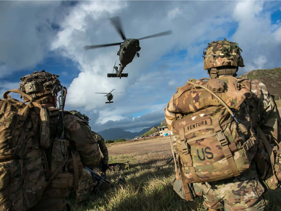 兩名身穿軍用裝備嘅士兵觀看直升機喺田野降落。