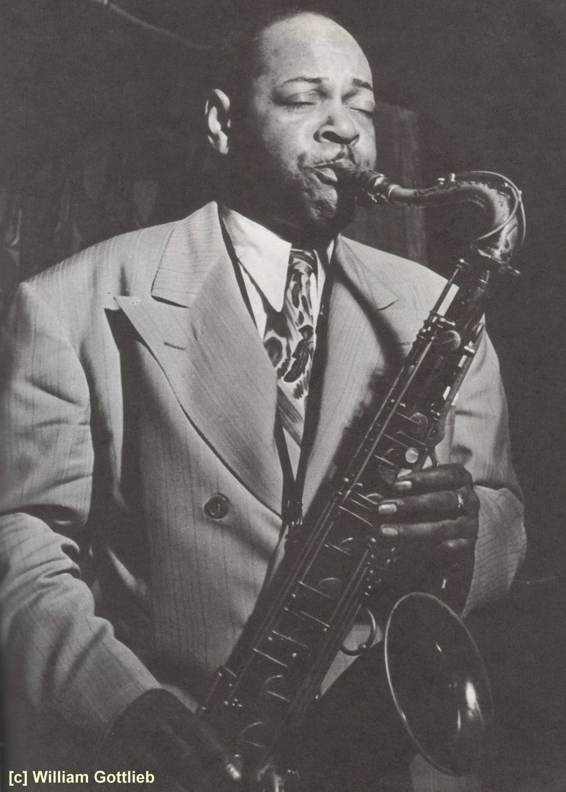 美國薩克斯風演奏家Coleman Hawkins 壁紙 — 一位身穿西裝的爵士音樂家在戲劇性的舞台燈光下熱情地演奏色士風。