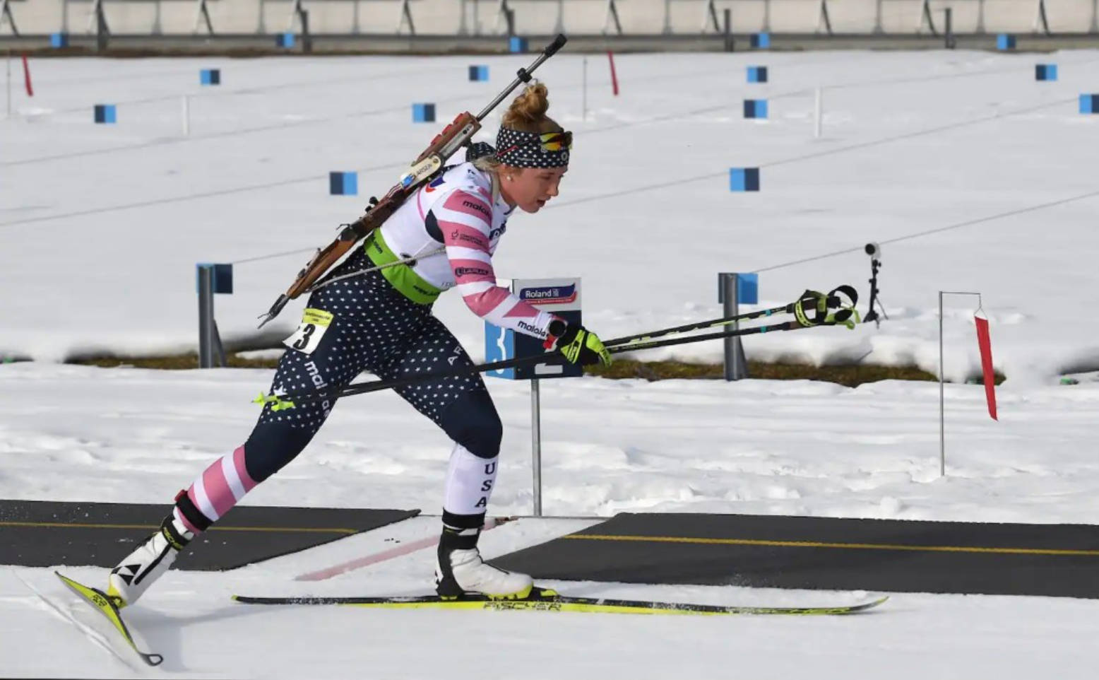 美國越野射擊運動員克洛伊·萊文斯 壁紙 — 一位女性冬季兩項運動員在雪地中滑雪前進，步槍掛在肩上。