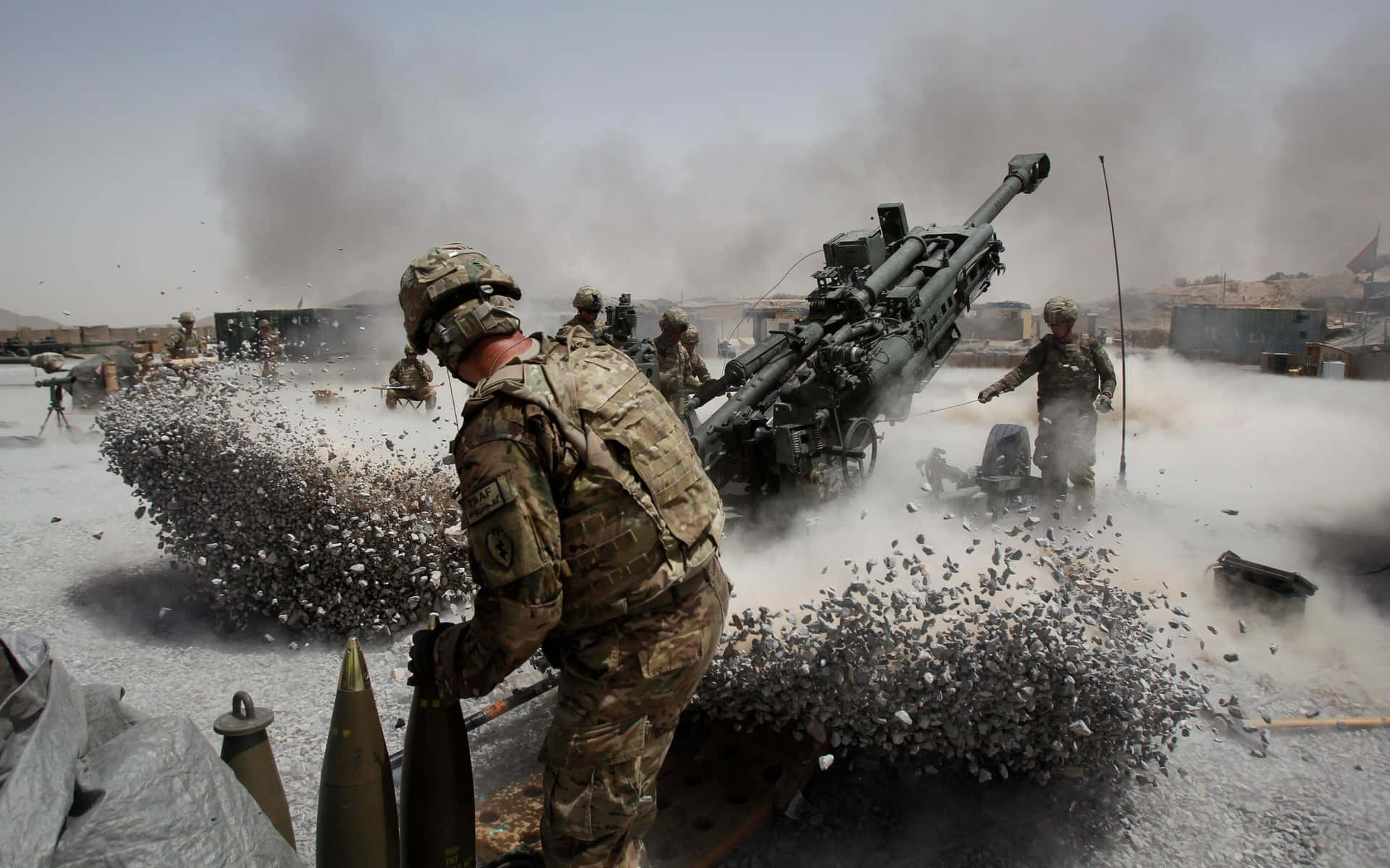 士兵在煙霧和碎片瀰漫的塵土飛揚戰鬥區域發射火炮。