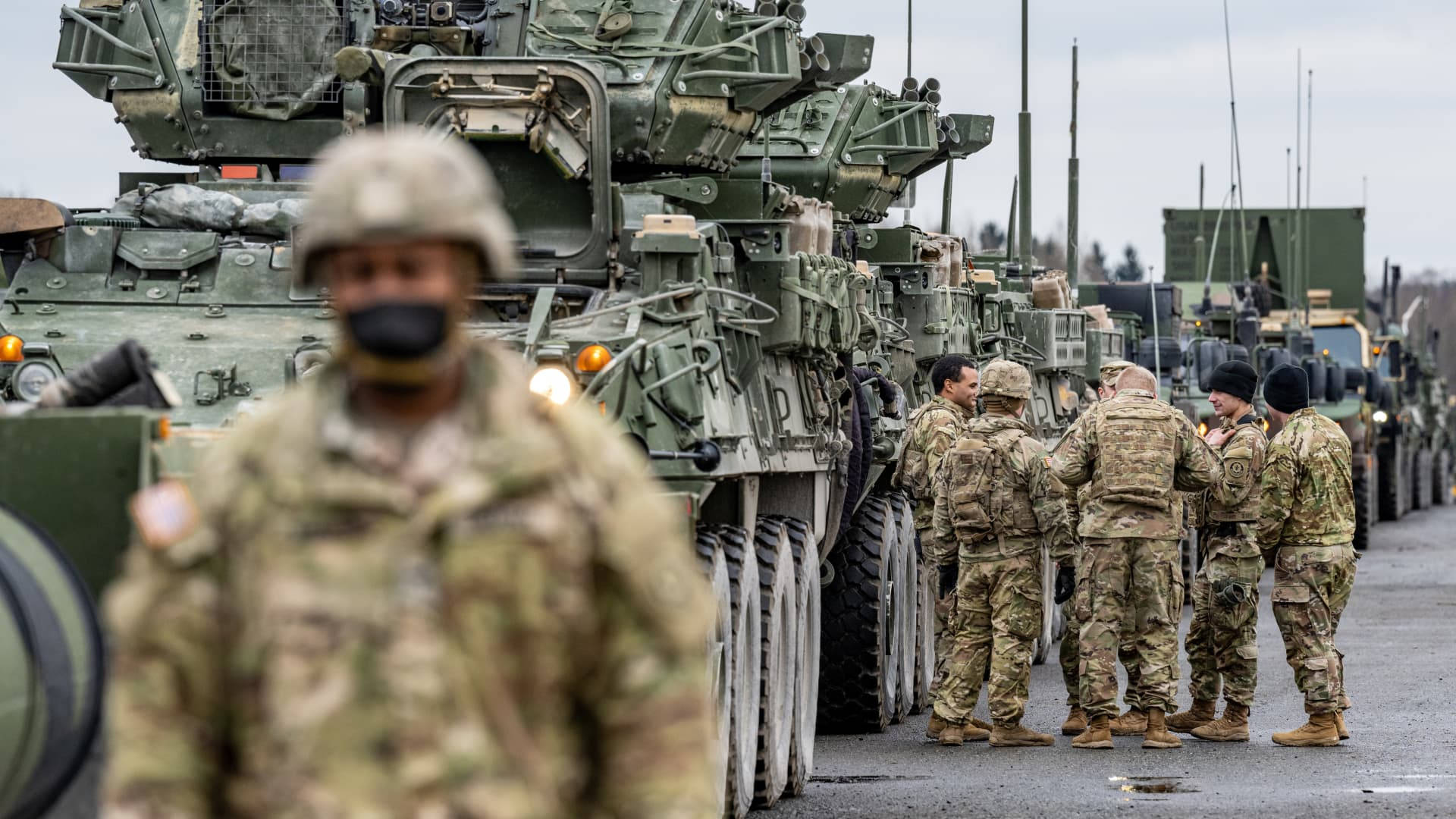 身穿迷彩裝備的士兵站在鋪砌道路上一排軍用裝甲車附近。